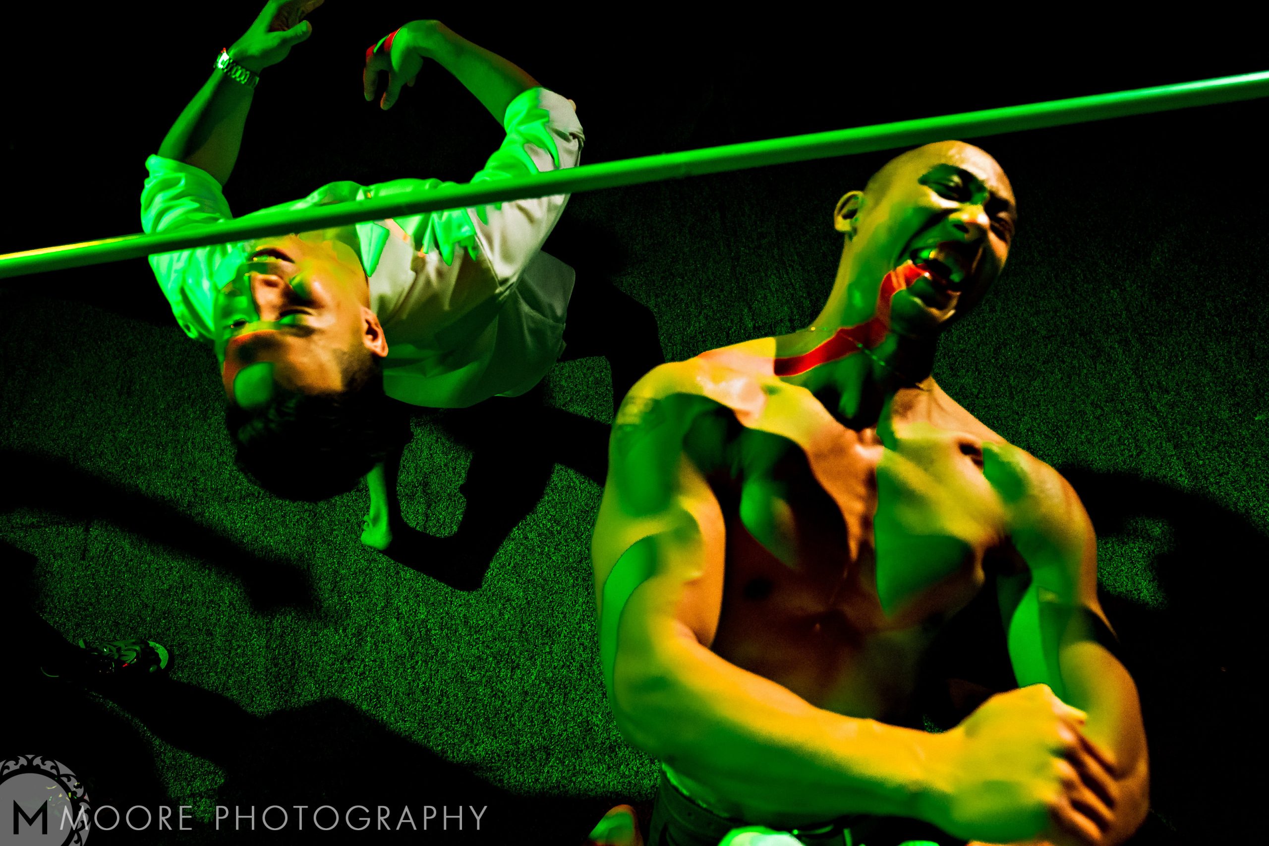 Two joyful men, one shirtless, one in white, dance under green lights at a Puerto Vallarta bash.