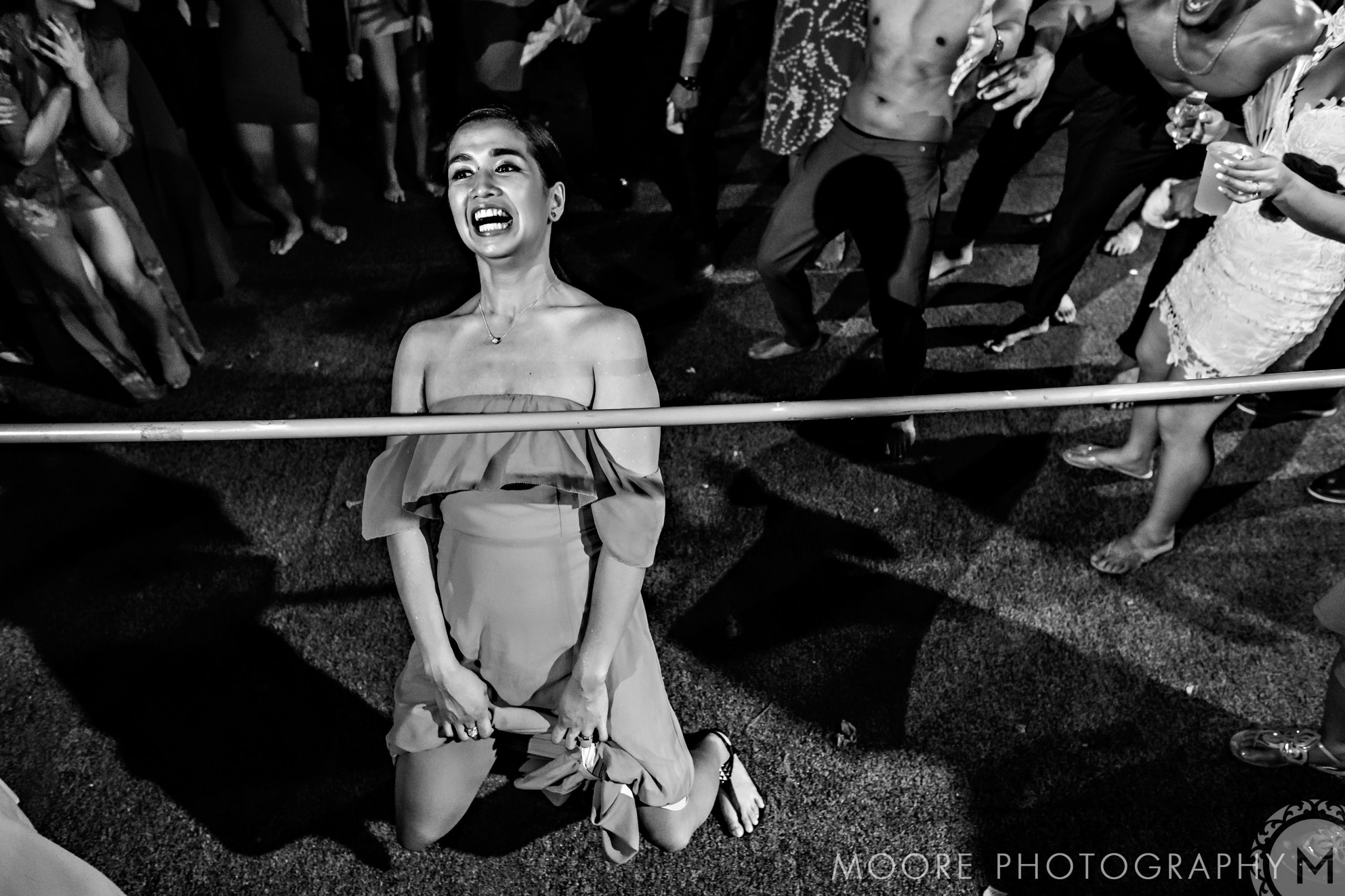 Woman smiling while bending under a limbo stick at a lively Puerto Vallarta party.