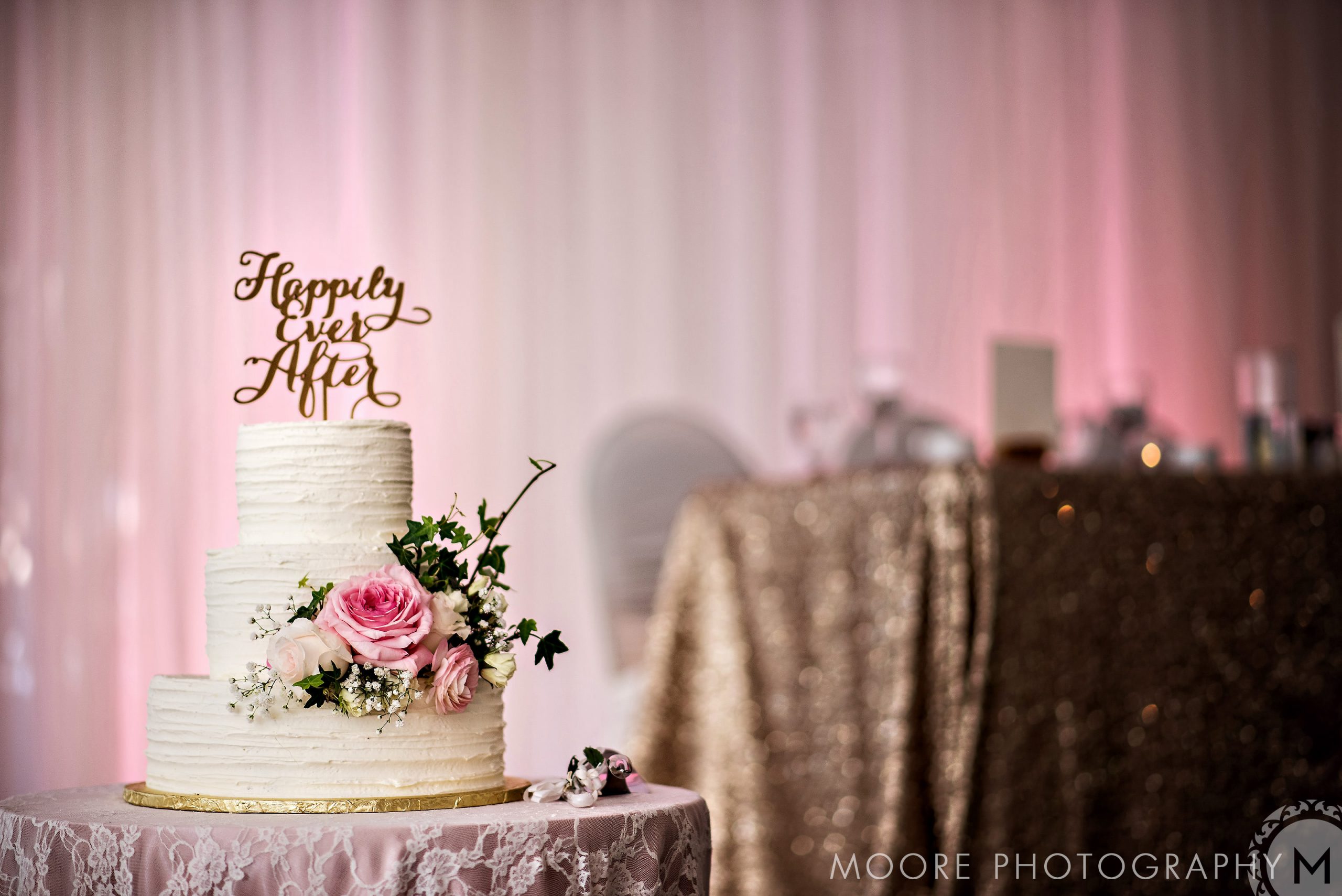 Three-tier cake with "Happily Ever After" topper, floral decor at Winnipeg wedding venues.