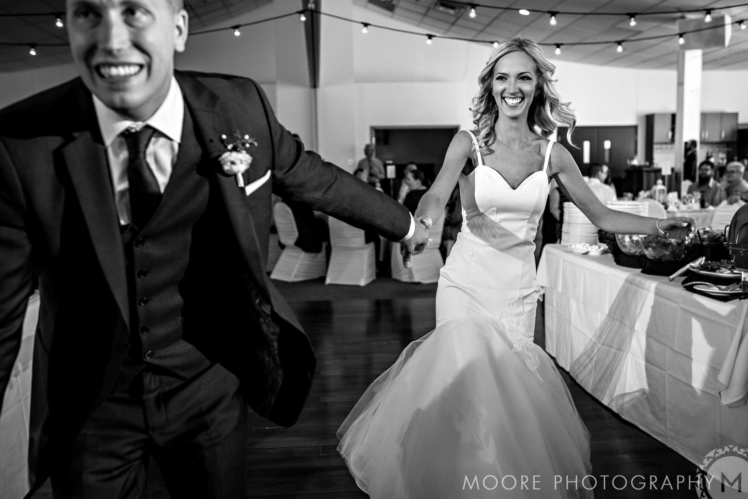 Bride and groom smiling, hand-in-hand in their wedding attire at the celebration hall.