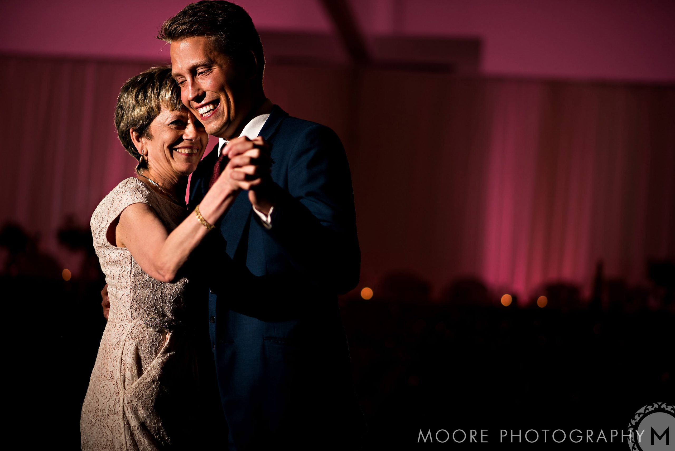 A woman and man smiling while dancing in elegant attire at a wedding celebration.