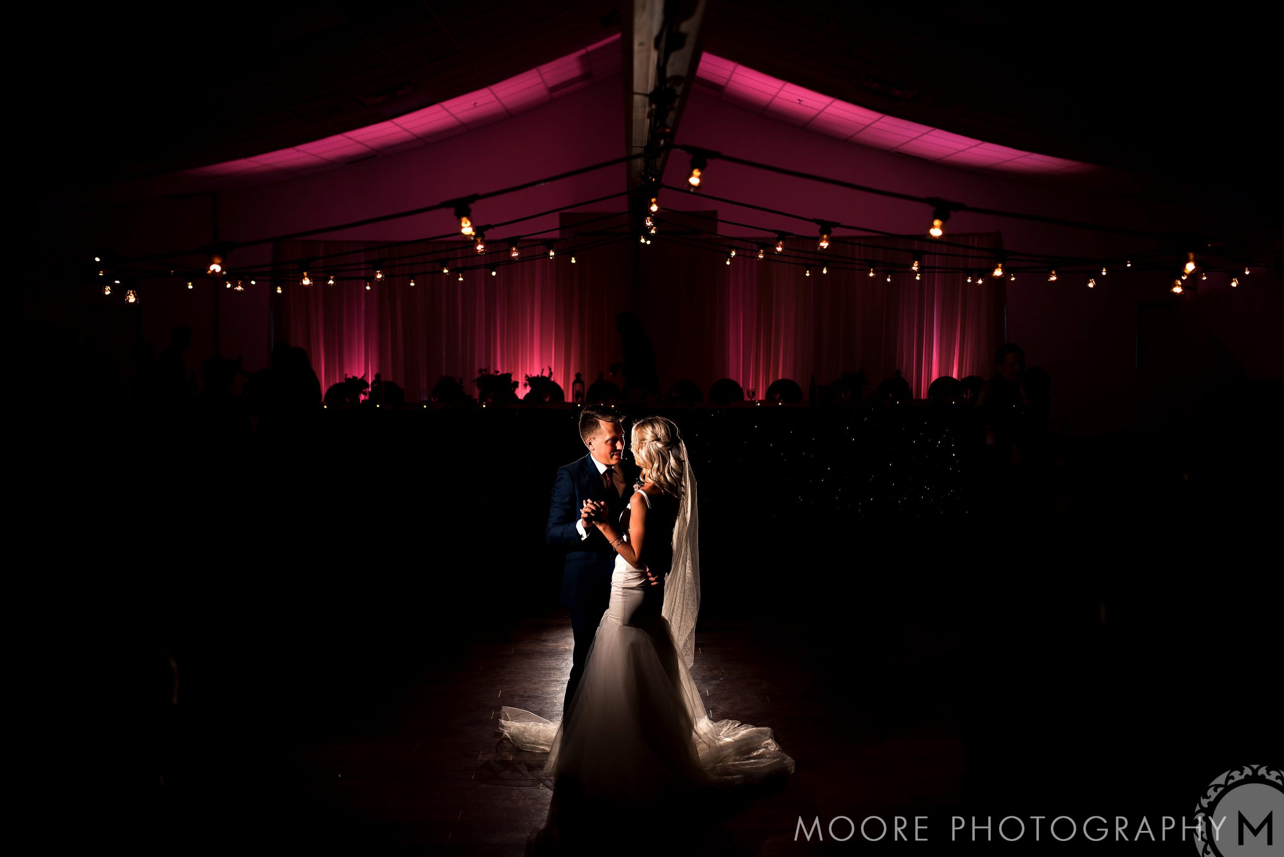Bride and groom dancing in a dimly lit venue during a wedding celebration with pink uplighting.