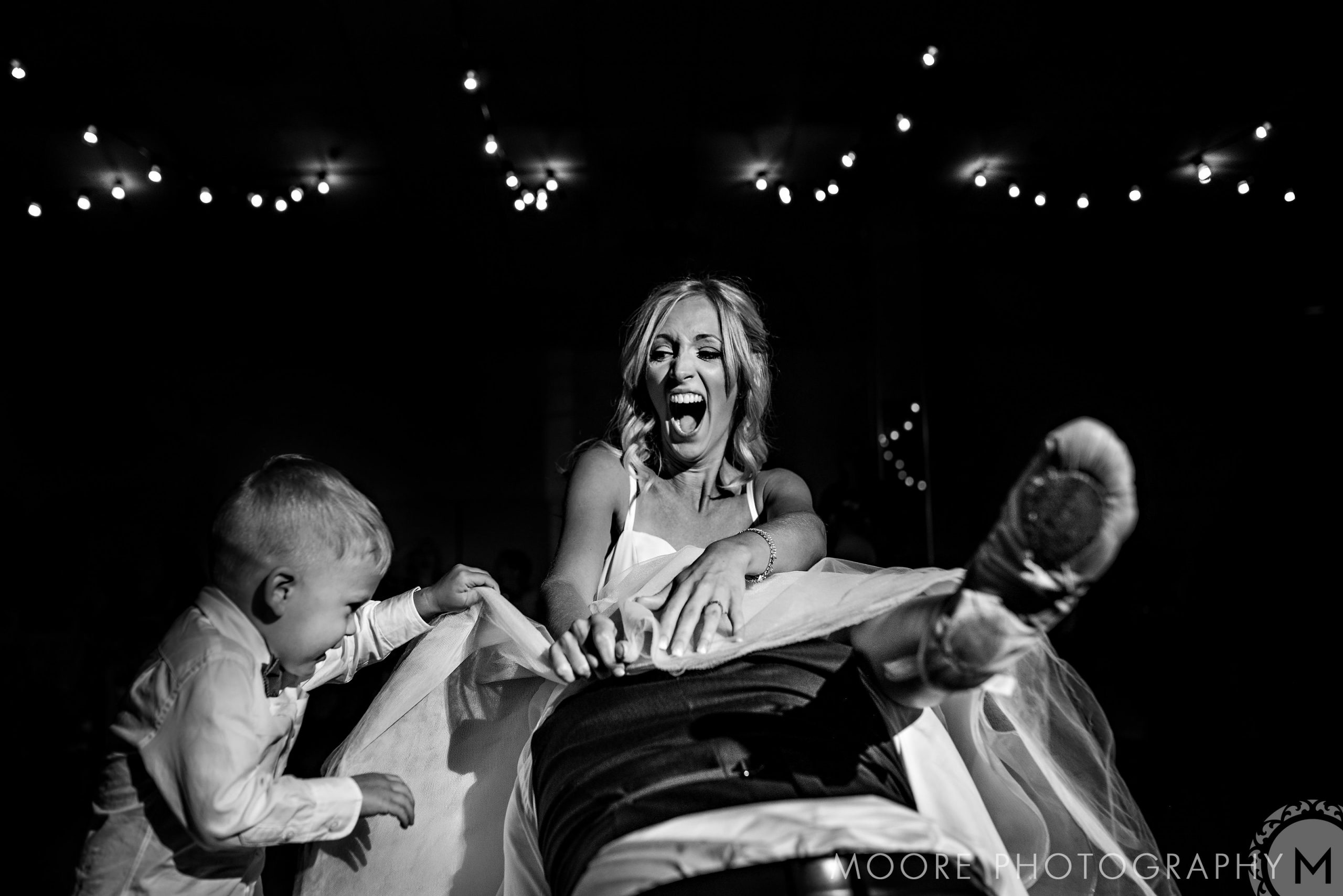 Bride laughing with child pulling her dress under Winnipeg wedding venue's string lights.