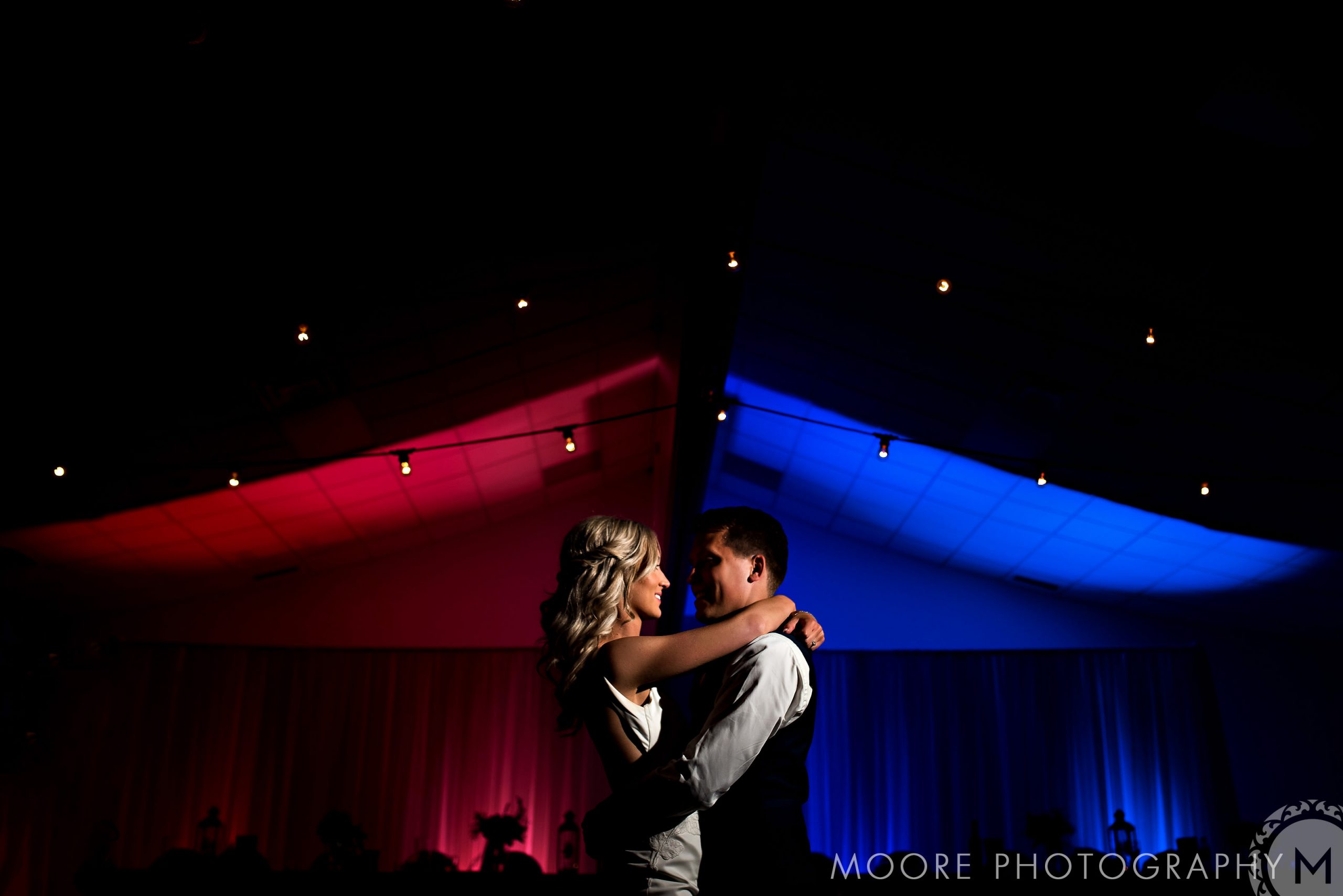 Couple dancing in a dimly lit Winnipeg wedding venue under red and blue lighting.