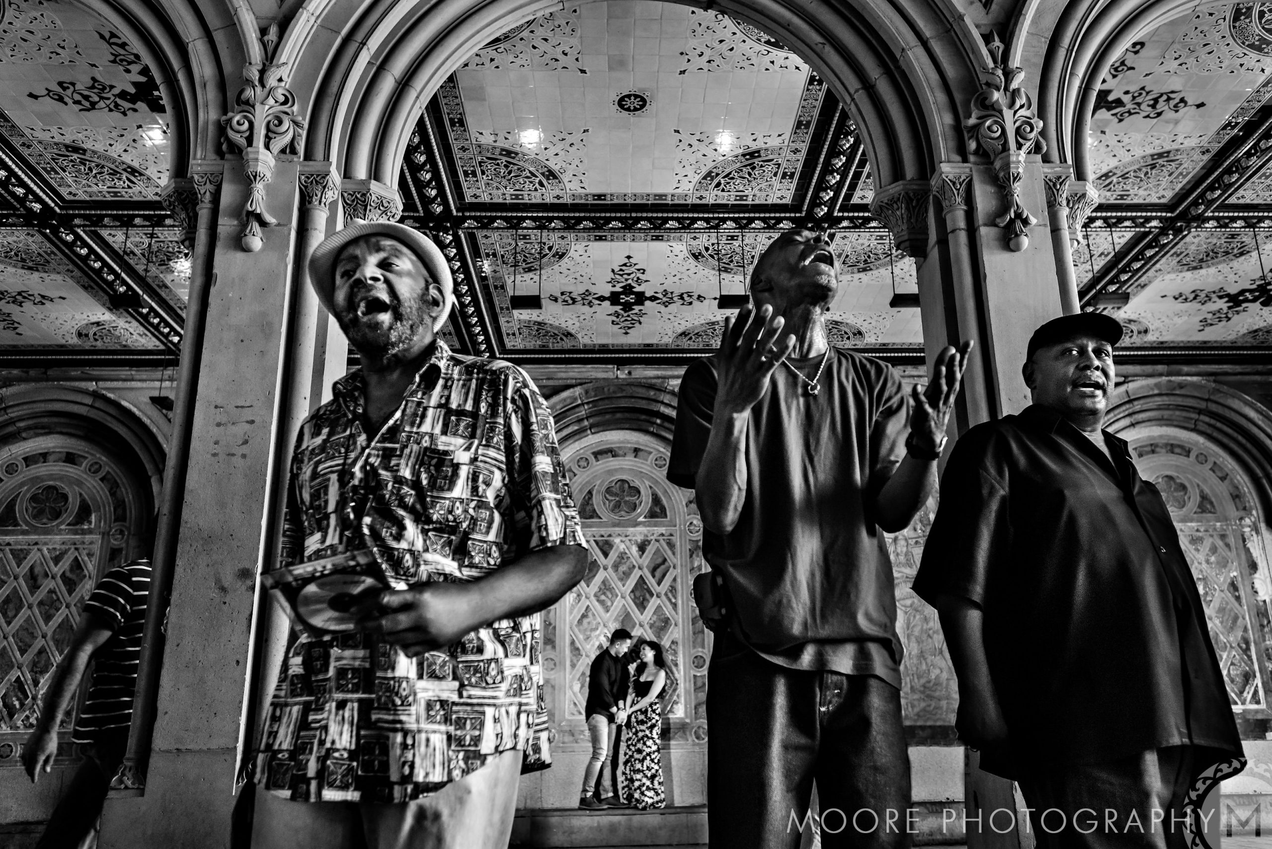 Three people singing under ornate arches, with a romantic NYC engagement in the background.