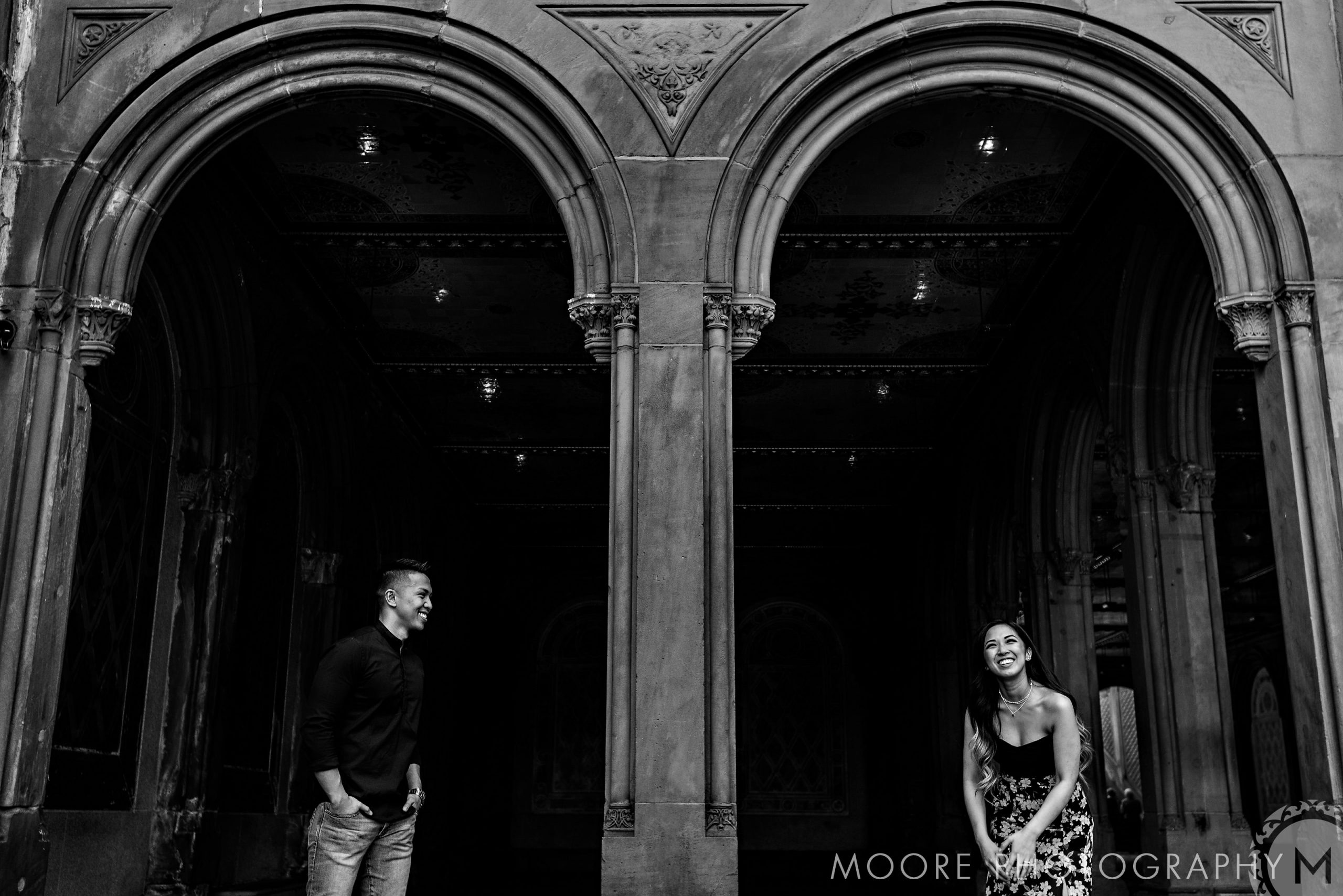 Couple smiling under ornate arches in a romantic NYC engagement photograph.