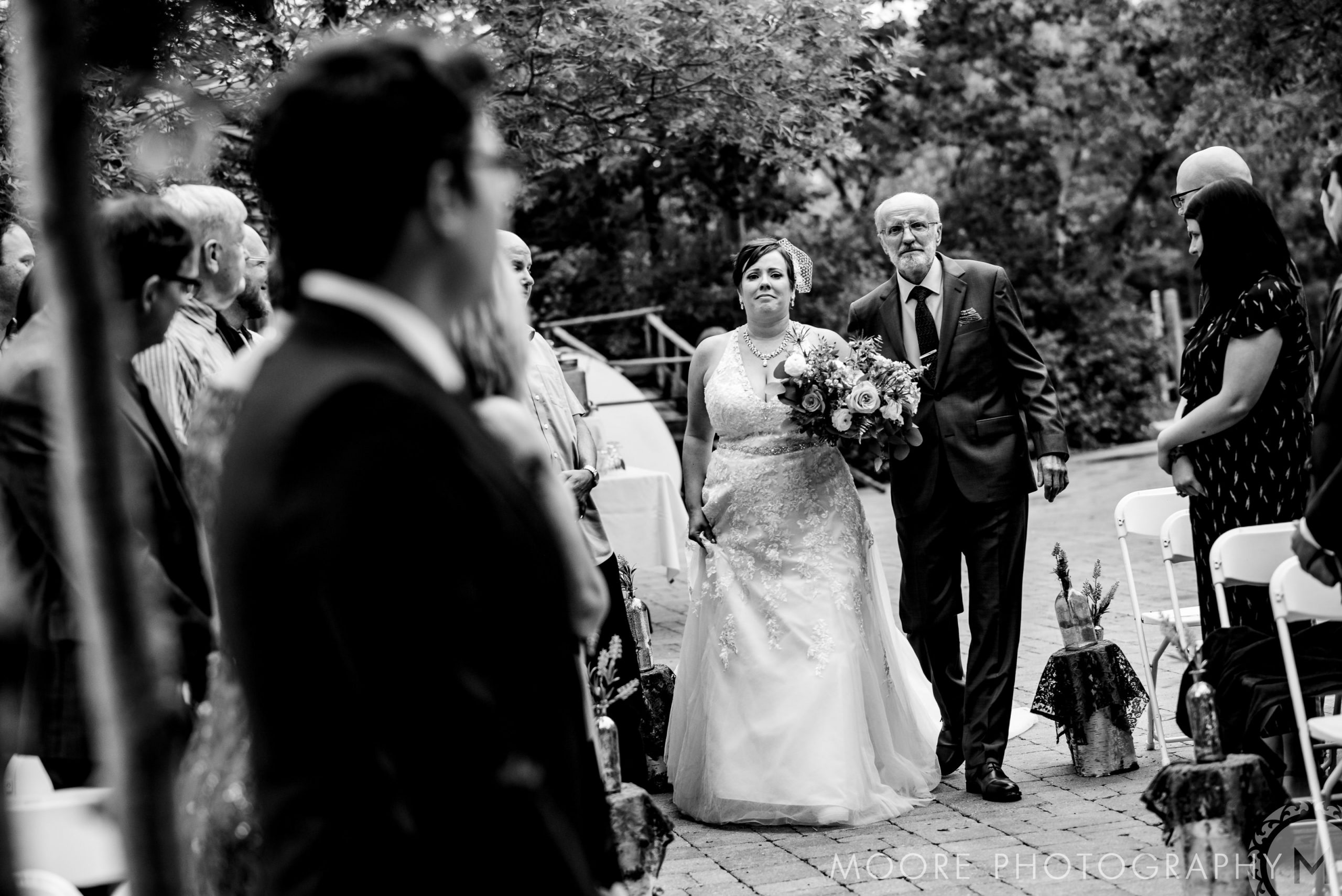 A bride walks down the aisle with an older man at a Winnipeg outdoor wedding ceremony.