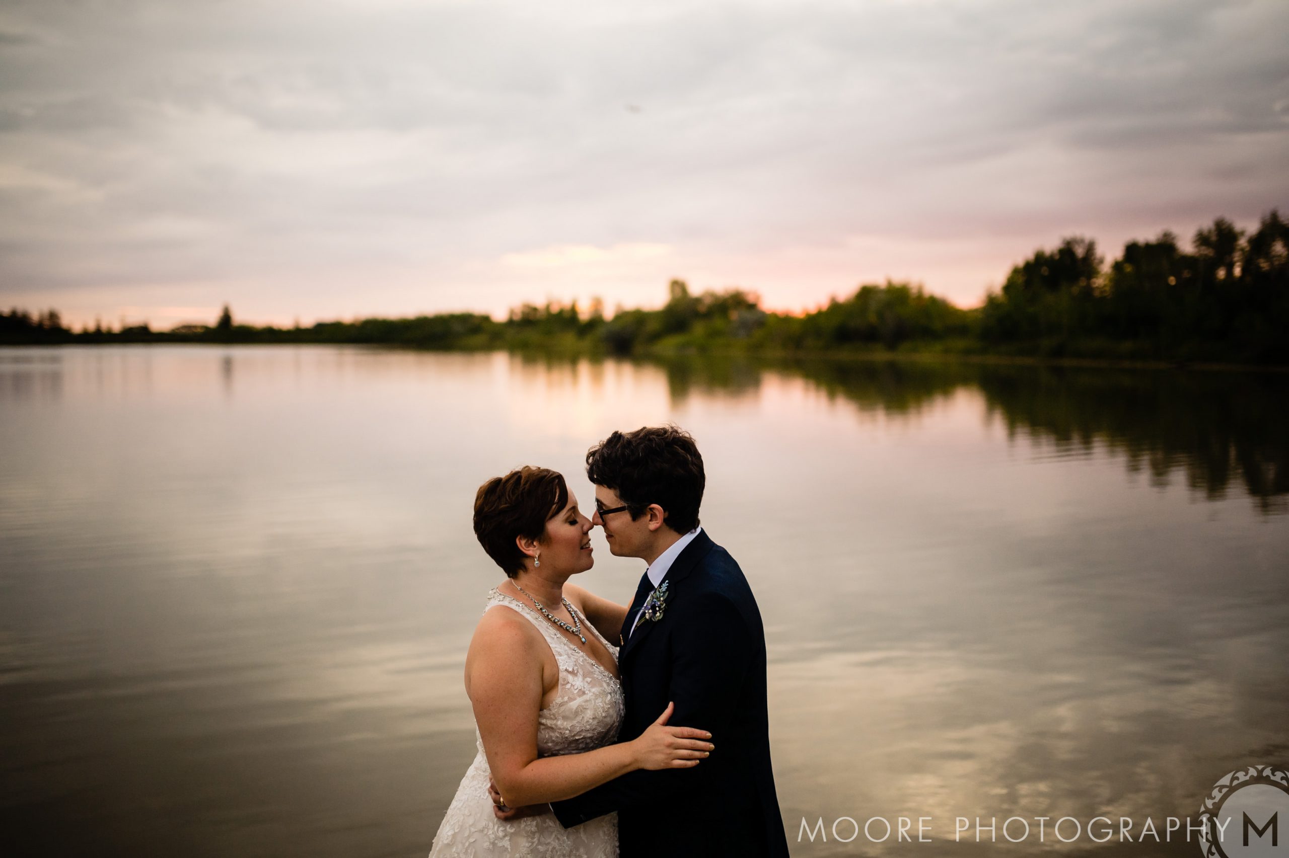 A couple embraces by a tranquil lake at sunset, a perfect Winnipeg wedding venue.