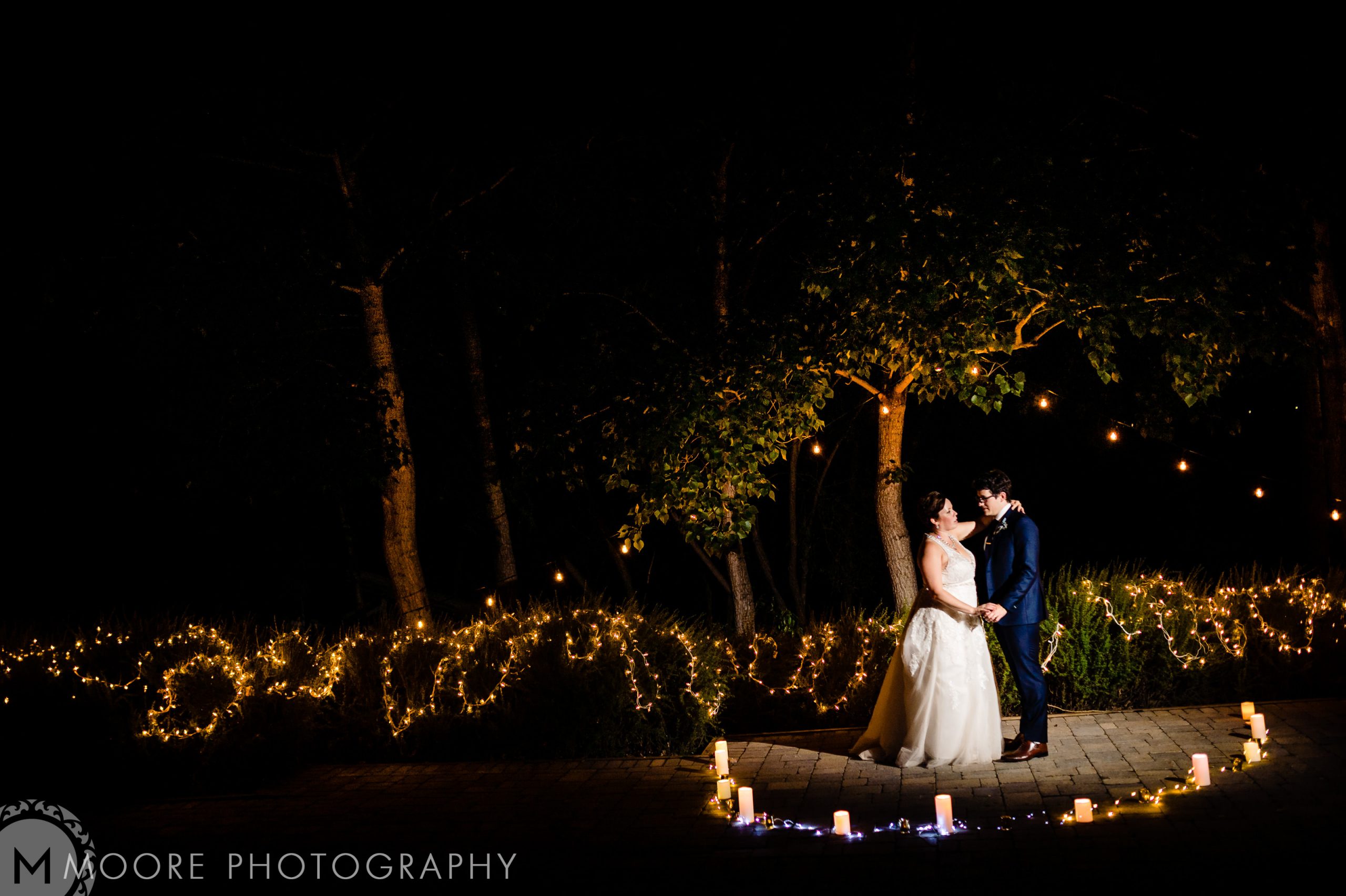 Bride and groom embrace under string-lit trees at Winnipeg wedding venues.