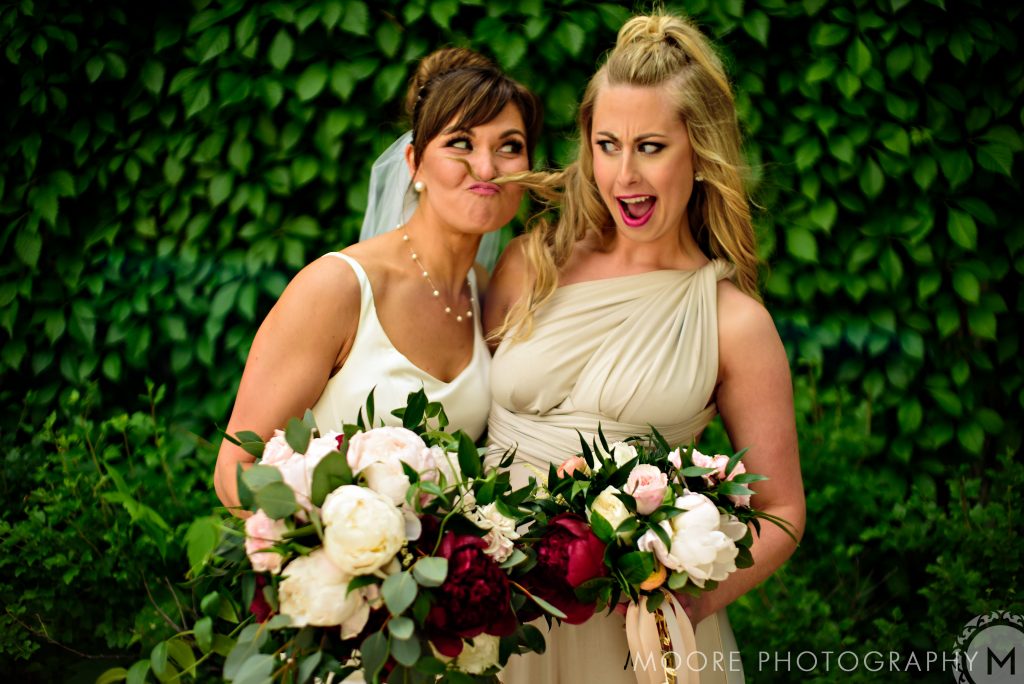 Bride and her bridesmaid being goofy in front of a vine wall in Winnipeg Manitoba