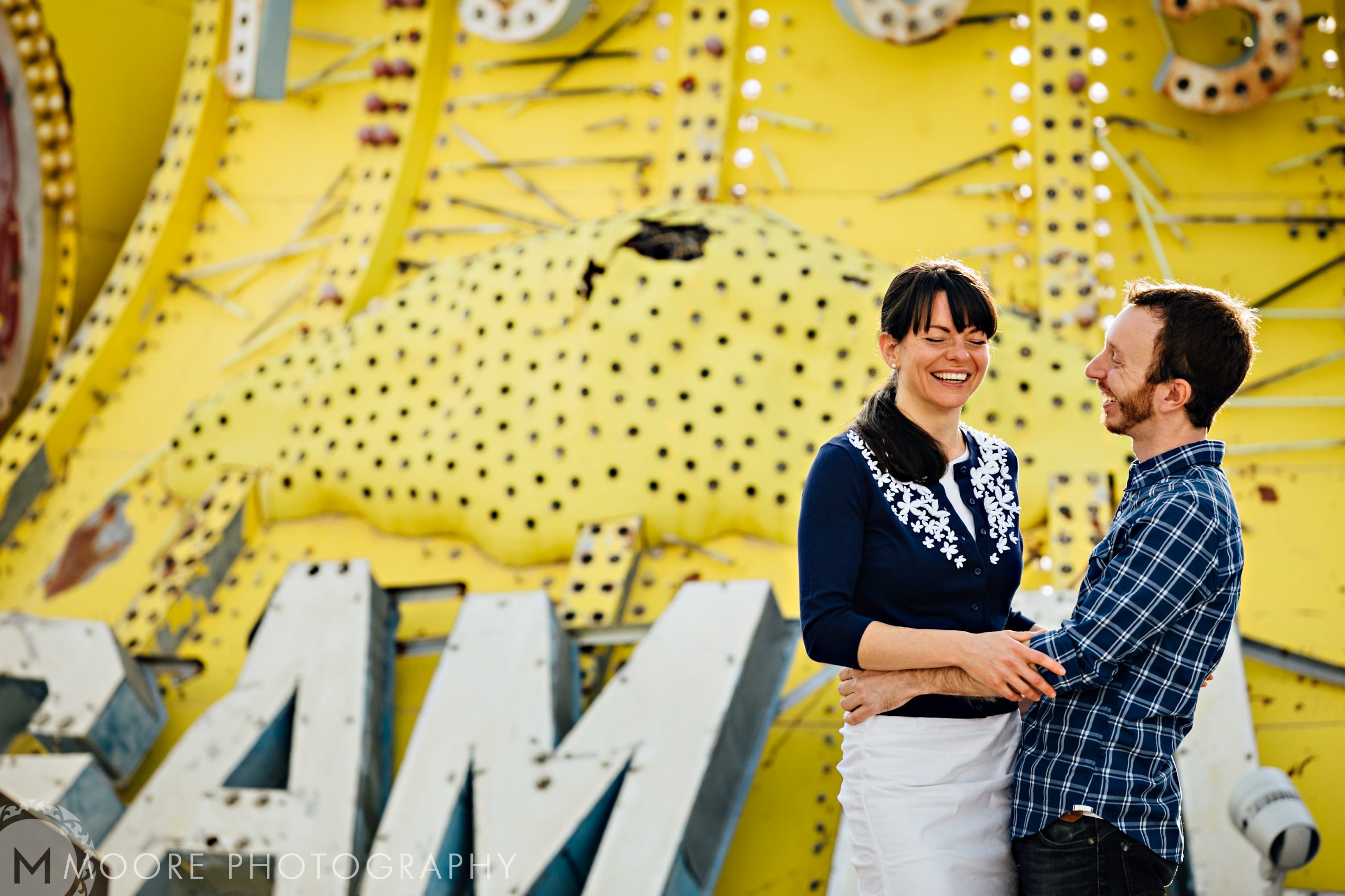 Couple beaming in front of a vintage yellow neon sign, perfect for destination wedding photography.
