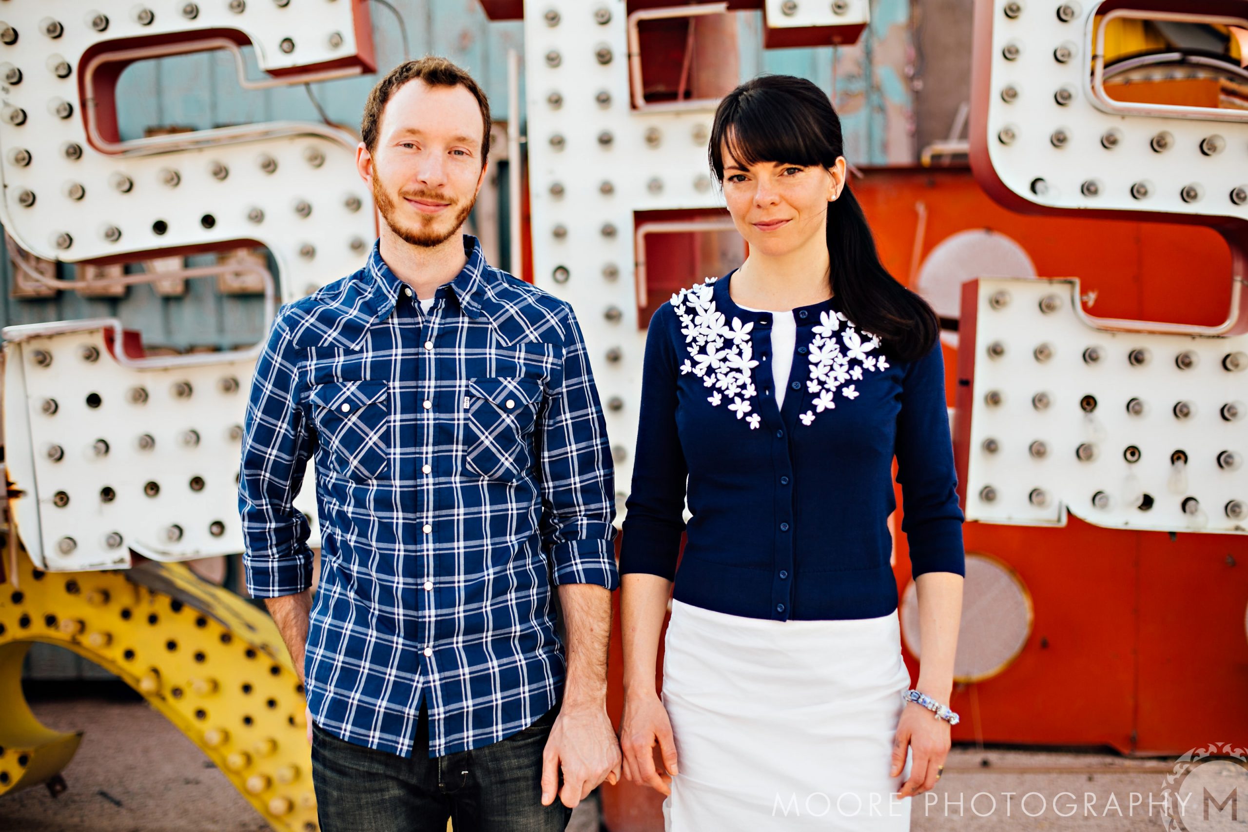 A couple holding hands by a vintage neon sign, perfect for destination wedding photography.