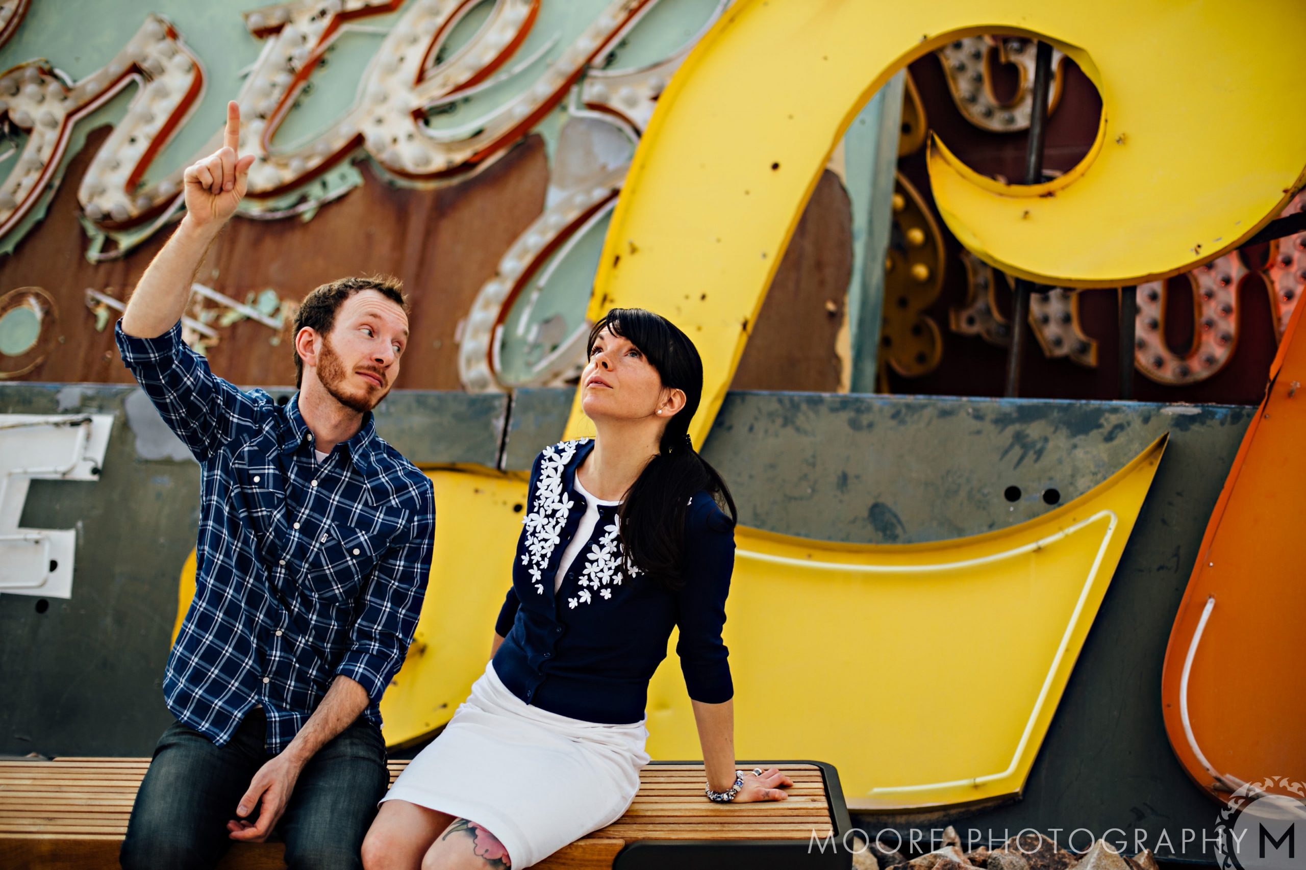 Couple looks up together, hinting at love; a retro sign backdrop adds charm.