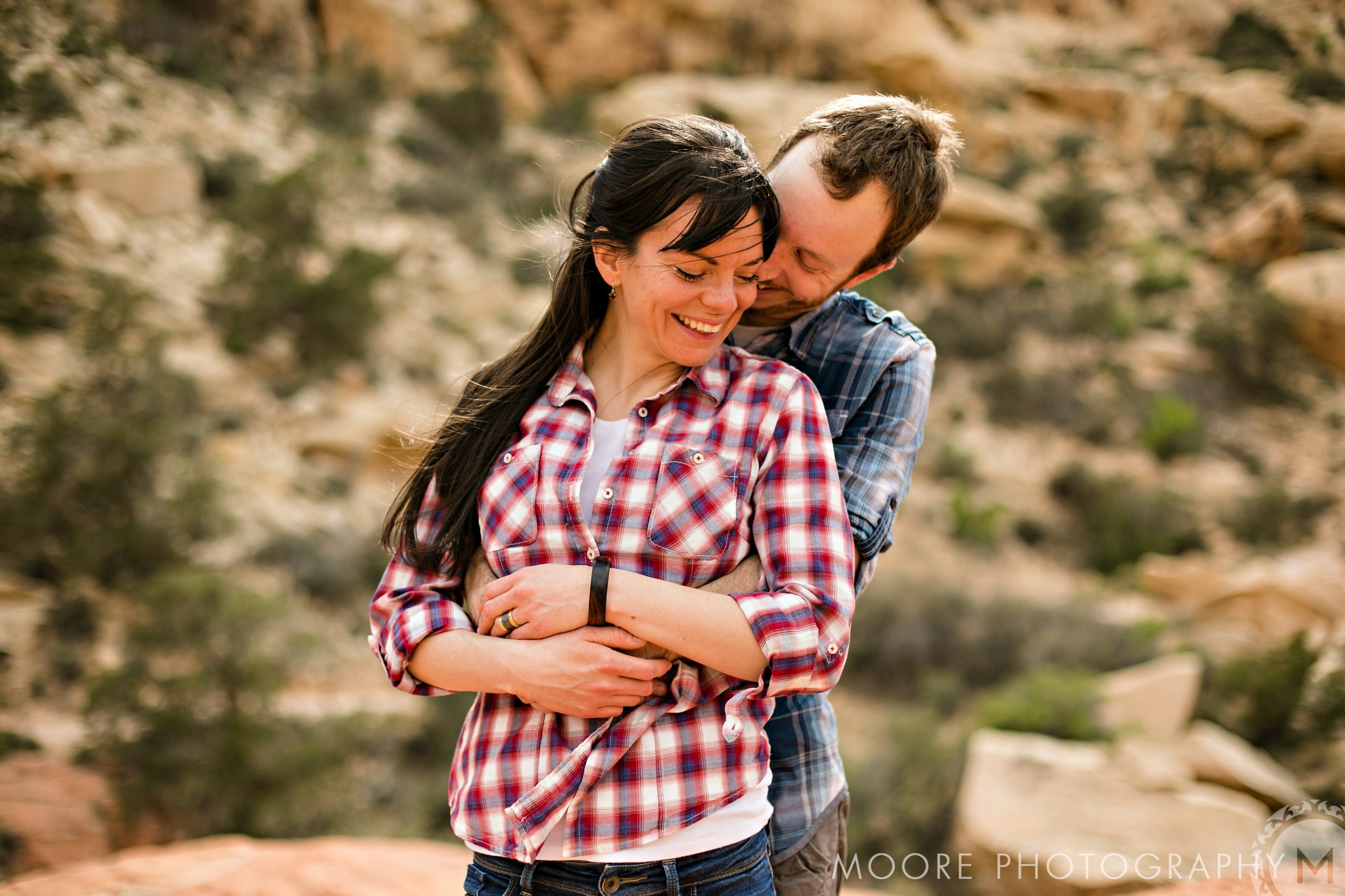 A couple embraces happily in a scenic, rocky destination wedding setting.