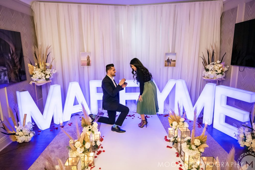 Man kneeling to propose to a woman with "Marry Me" sign, dreaming of Winnipeg wedding venues.