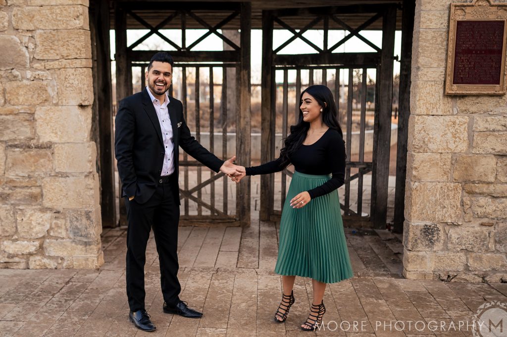 And engaged couple, holding hands, and laughing for a photo in front of upper Fort Gary in Winnipeg Manitoba