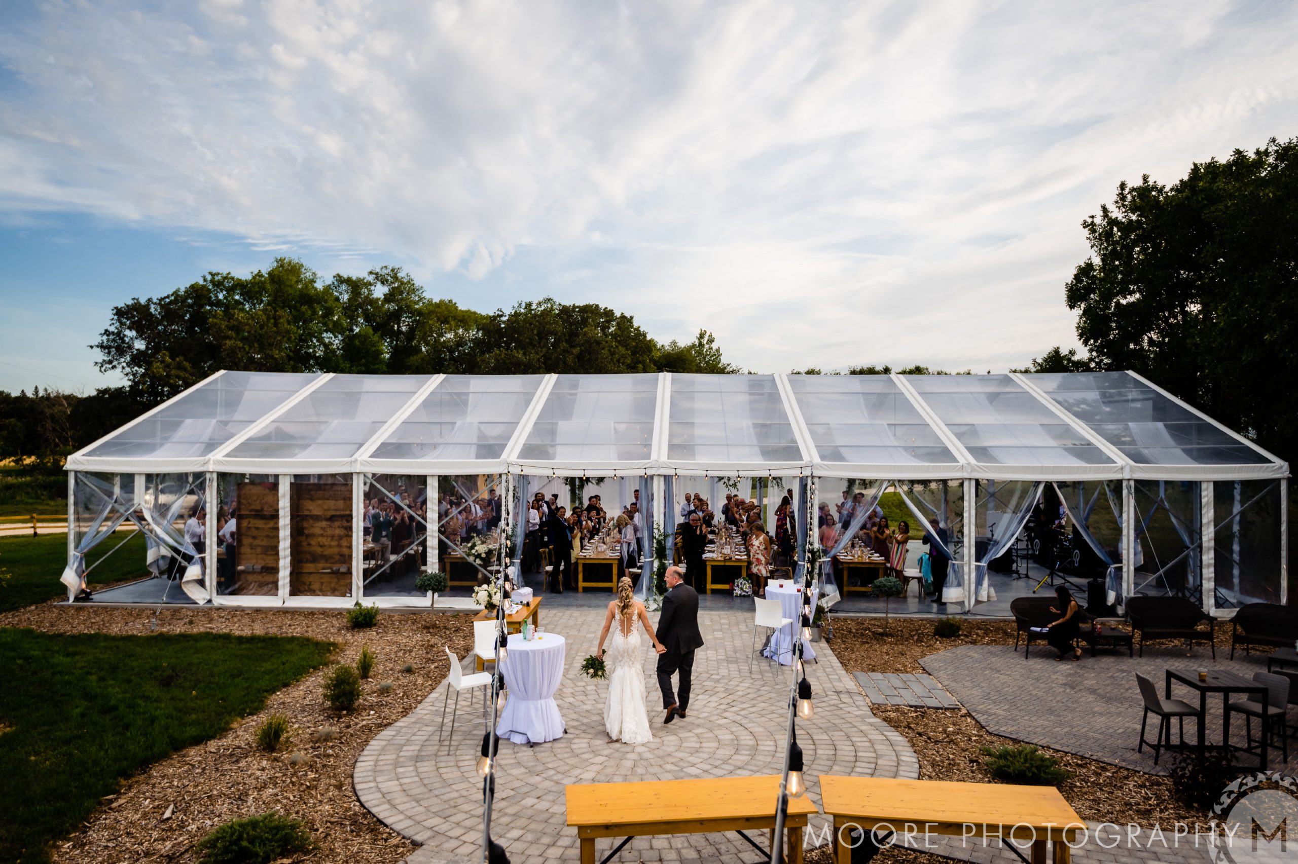 Outdoor wedding reception under a large transparent tent with guests in Winnipeg venues.