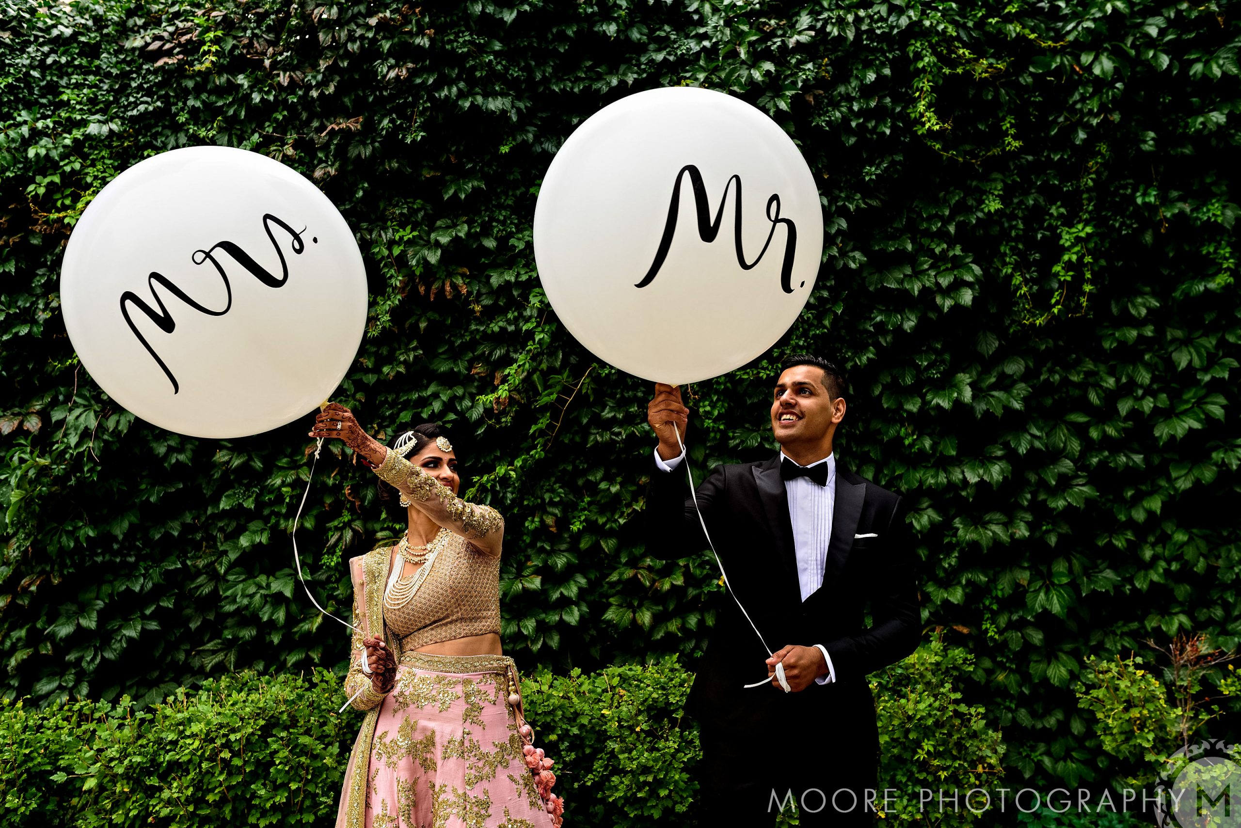 Couple with "Mrs." and "Mr." balloons in lush green Winnipeg wedding venue.