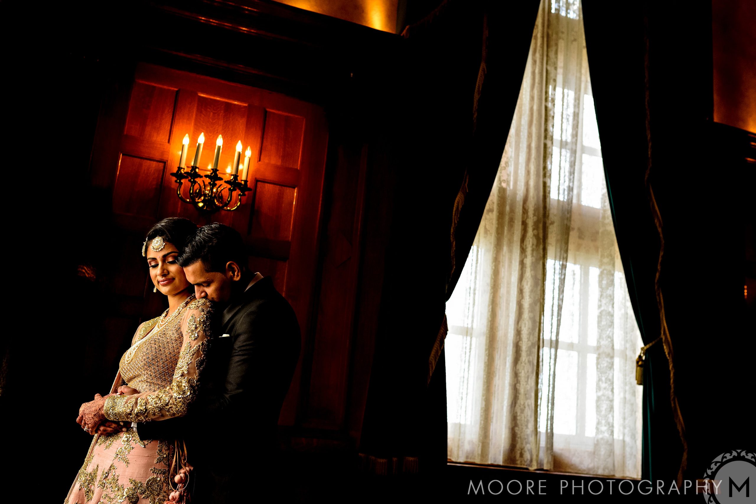 Couple embracing in elegant attire at a Winnipeg wedding venue with glowing chandelier.