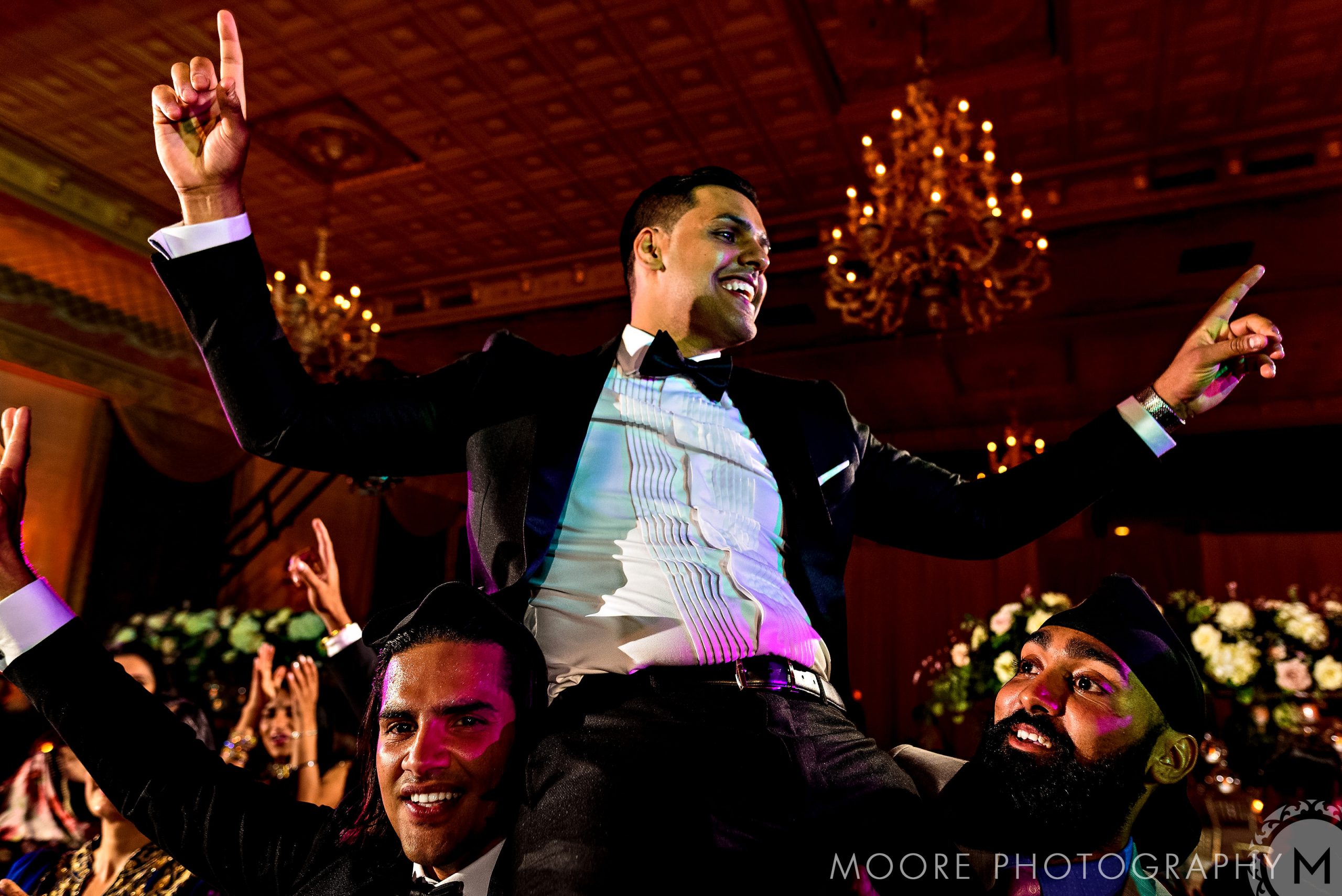 Man in suit celebrating, lifted by two others at a lively event in Winnipeg wedding venues.