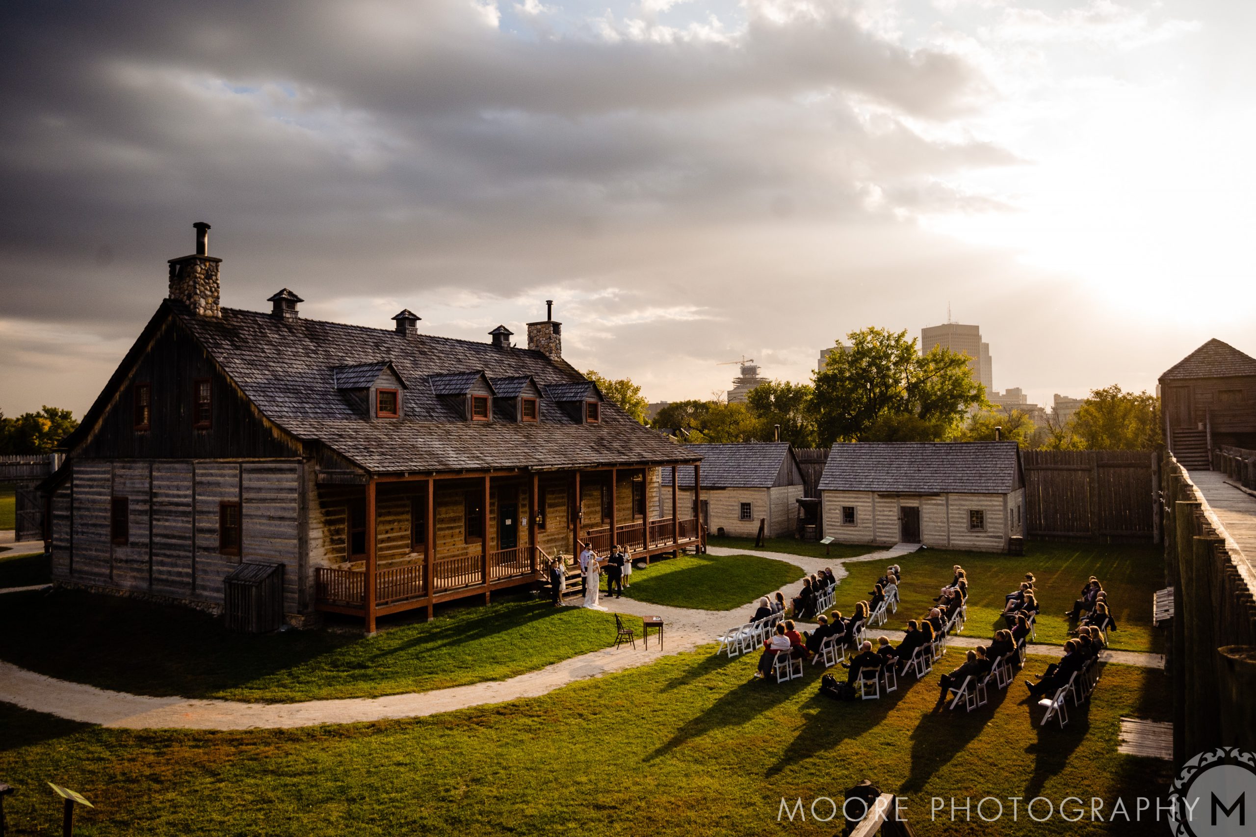 Outdoor wedding at a historic wooden fort in Winnipeg under dramatic clouds and sunlight.