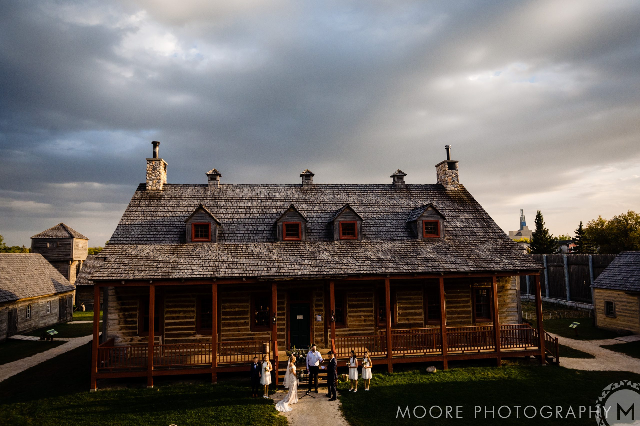 Historic wooden building, a gem among Winnipeg wedding venues, with people outside under a cloudy sky.
