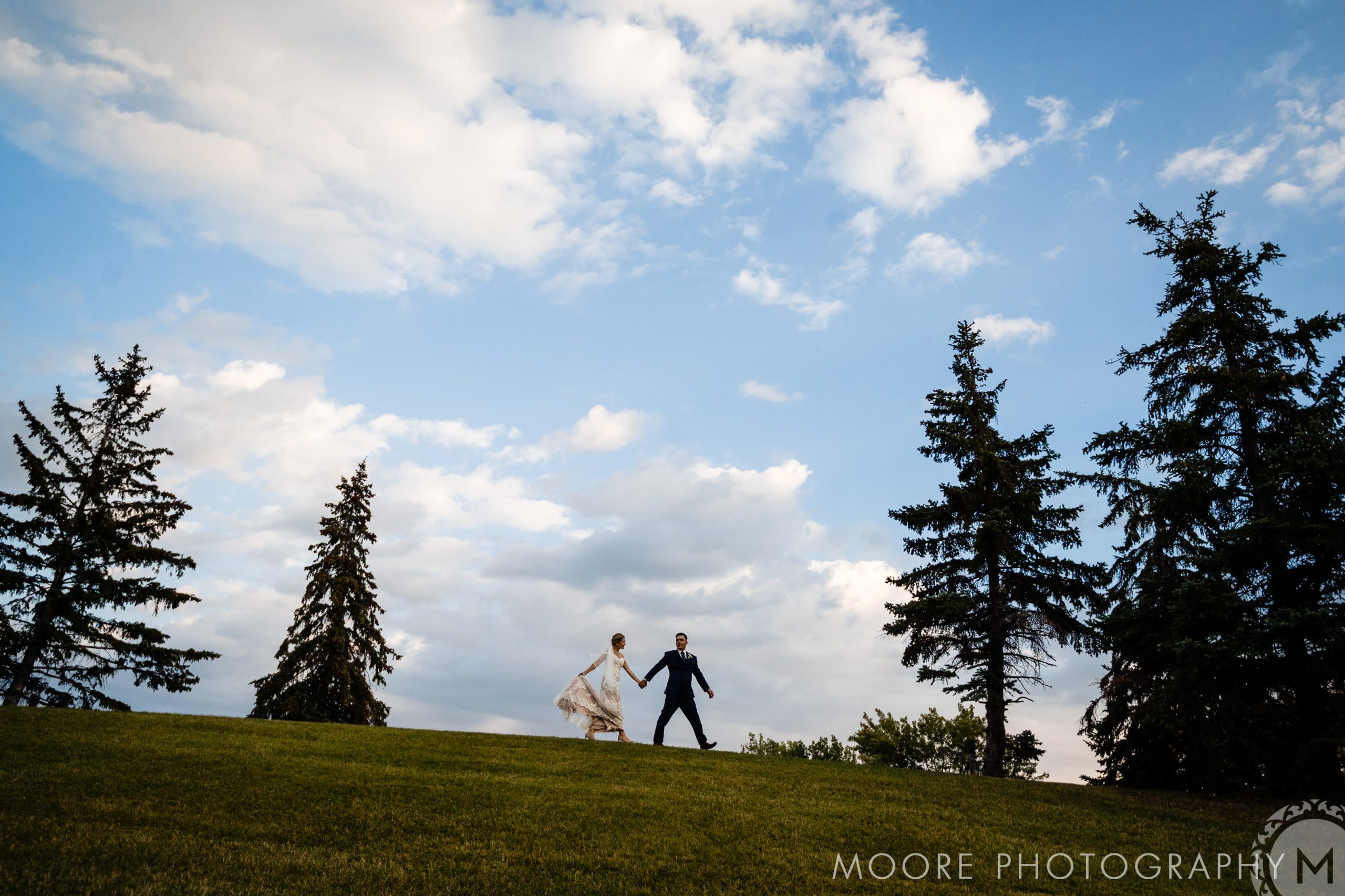 Couple strolls hand in hand on a grassy hill, dreaming of Winnipeg wedding venues.