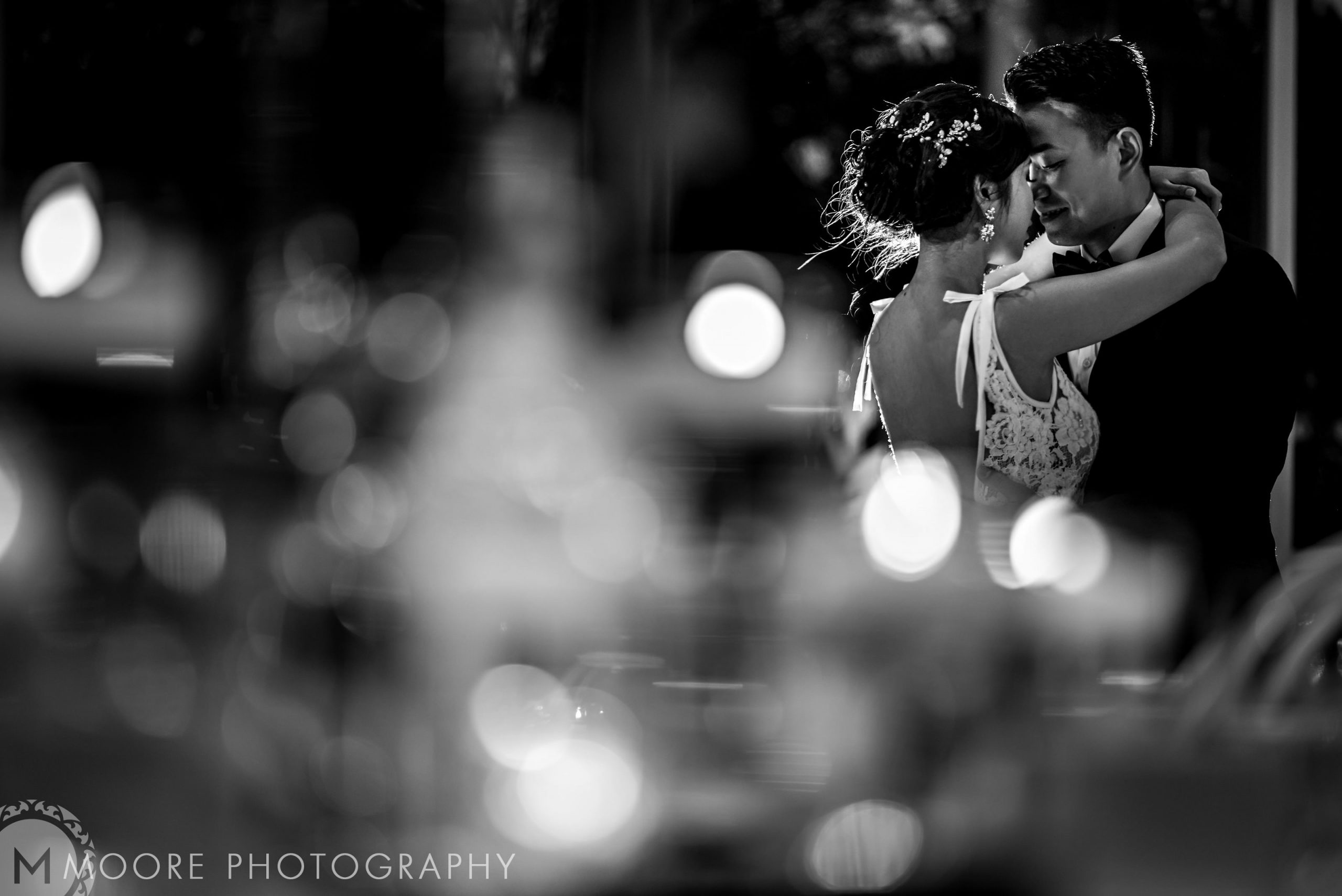 Bride and groom in an intimate embrace at a Winnipeg wedding venue, blurred lights foreground.