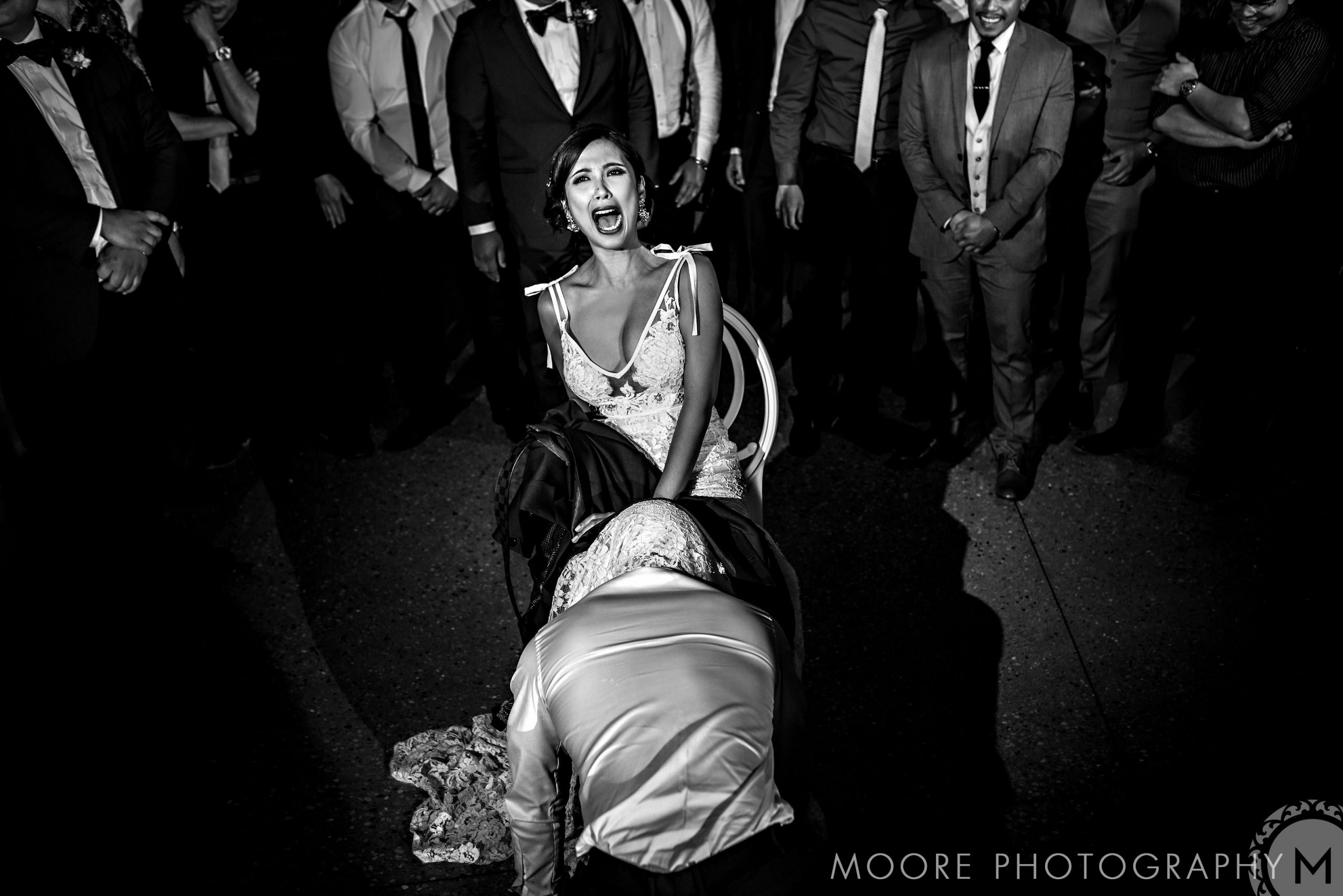 Bride laughing as groom retrieves garter, captured in black and white at a Winnipeg wedding.