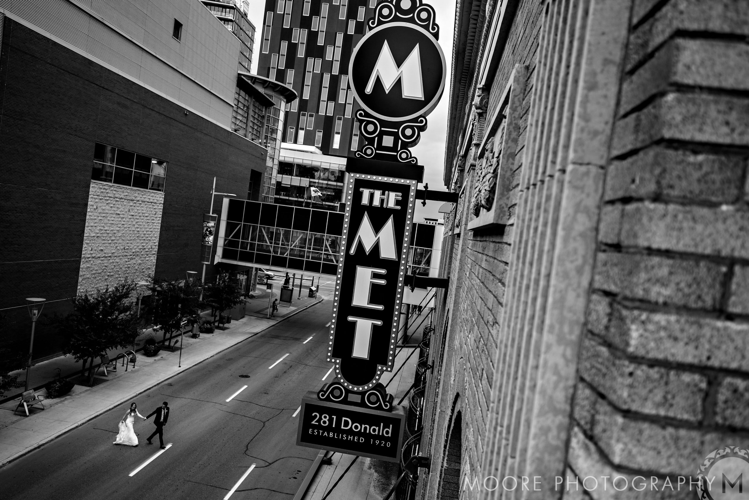 Bride and groom cross street by The MET in a timeless Winnipeg wedding scene.