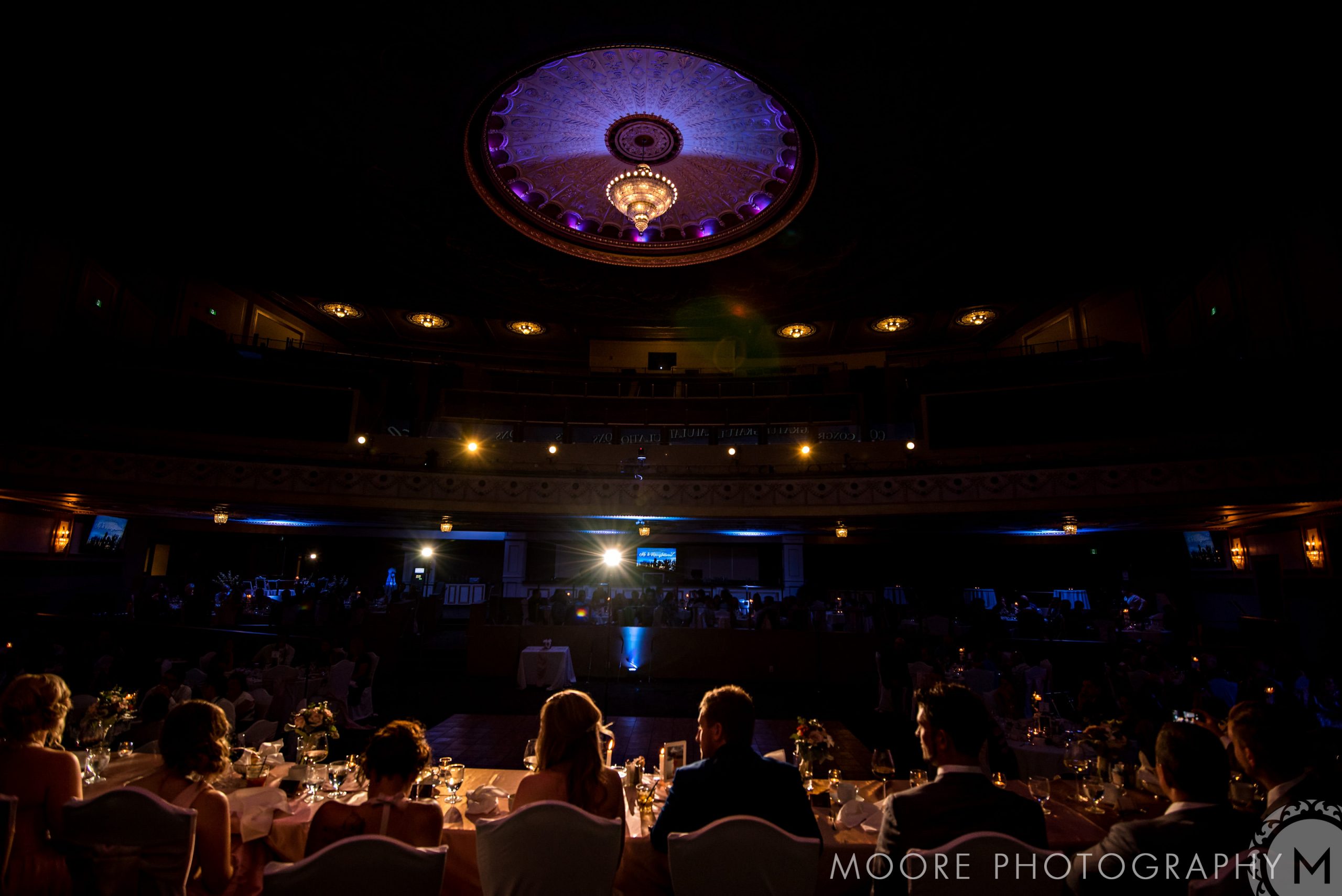 Guests seated at a dimly lit Winnipeg wedding venue under an ornate, illuminated ceiling.