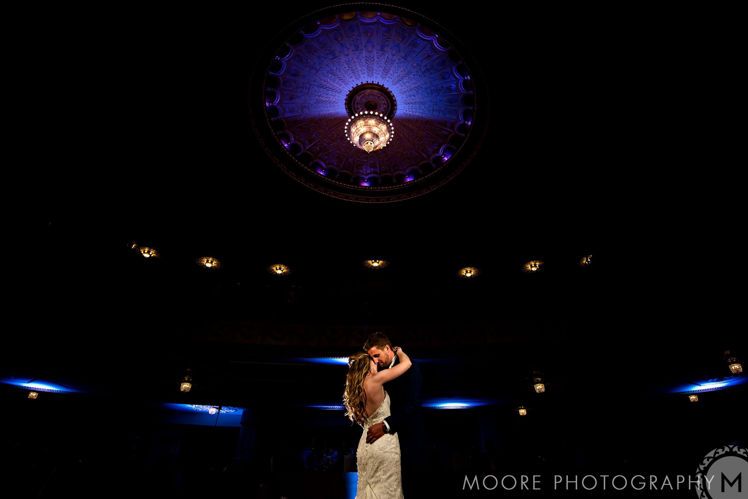 Couple dancing in a dimly lit room under ornate lights at a Winnipeg wedding venue.