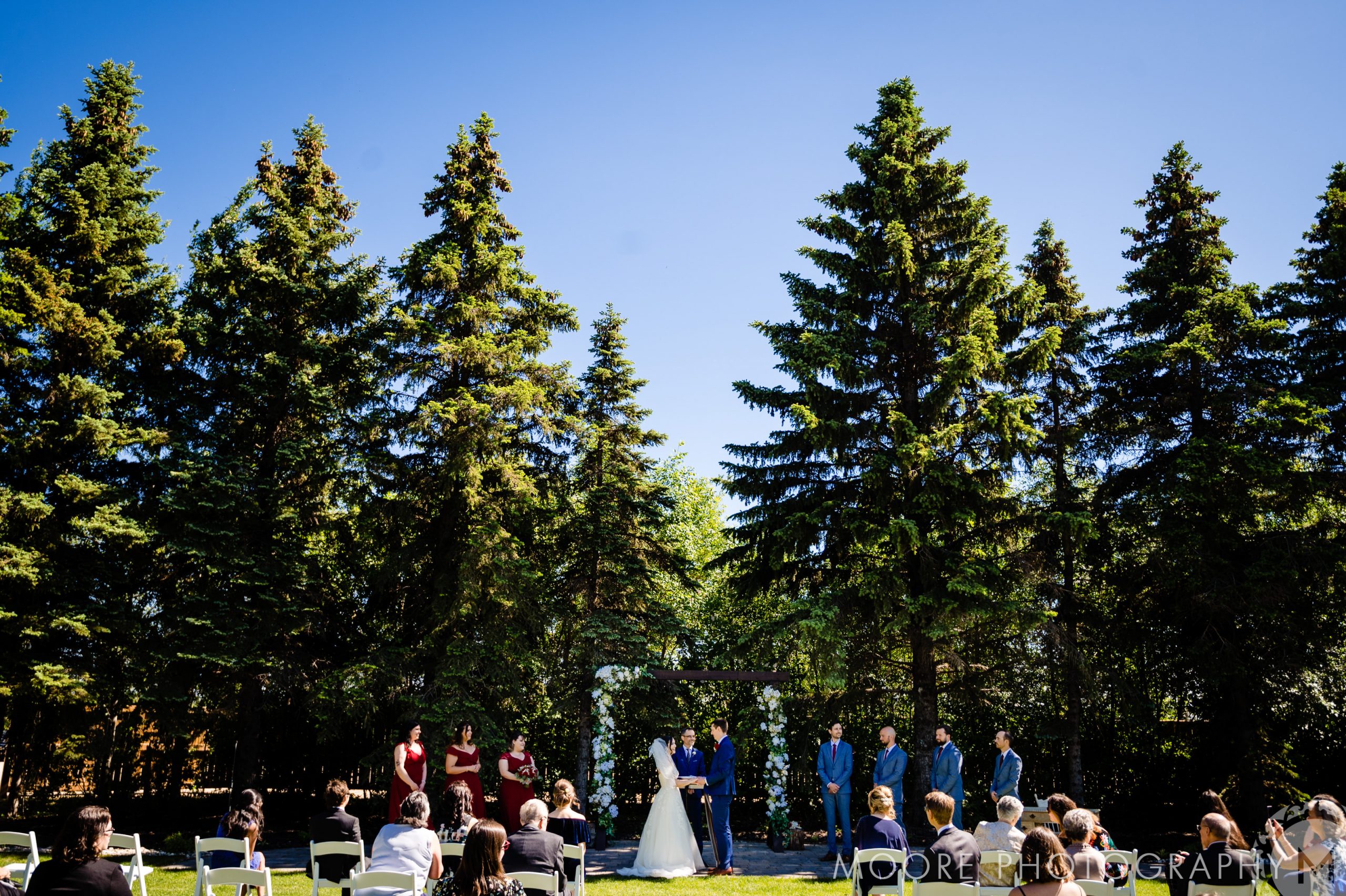 Under tall trees, a charming Winnipeg wedding venue hosts the couple and seated guests.