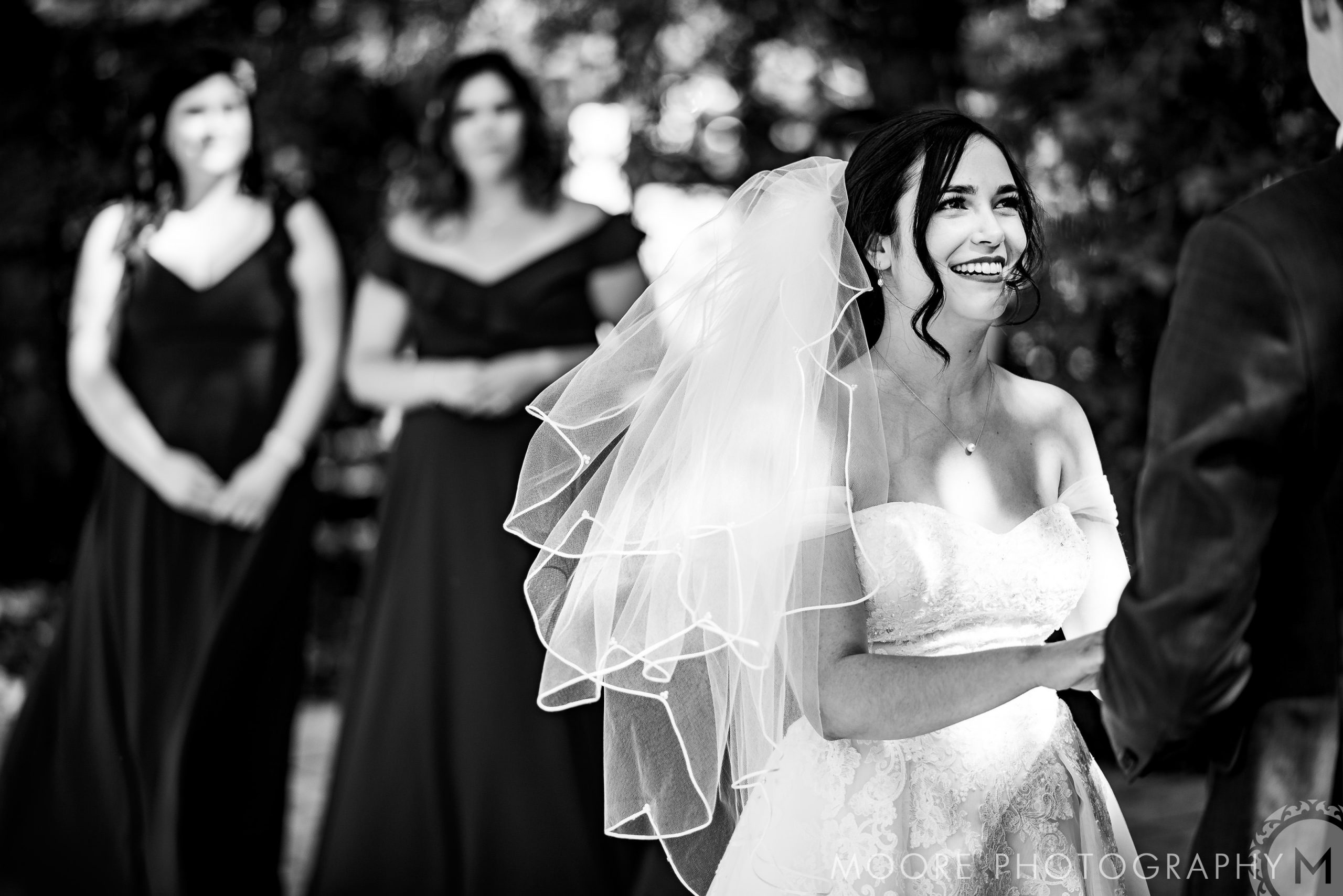 Bride beaming at Winnipeg wedding, two bridesmaids stand joyfully in the background.