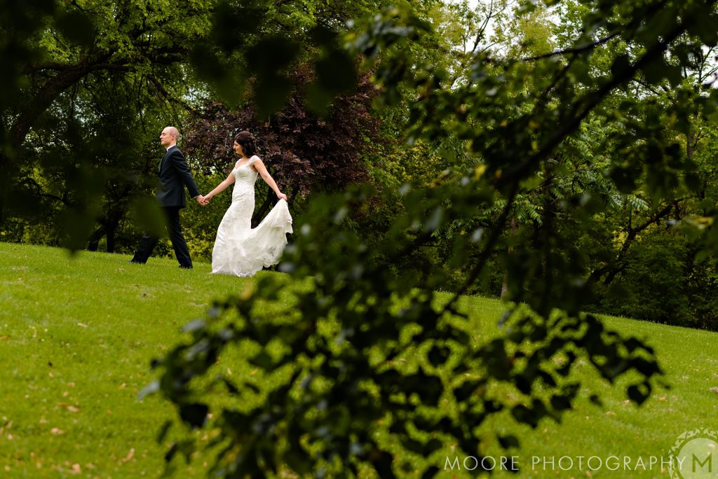 Bride and groom, walking and holding hands in a green park in downtown Winnipeg Manitoba