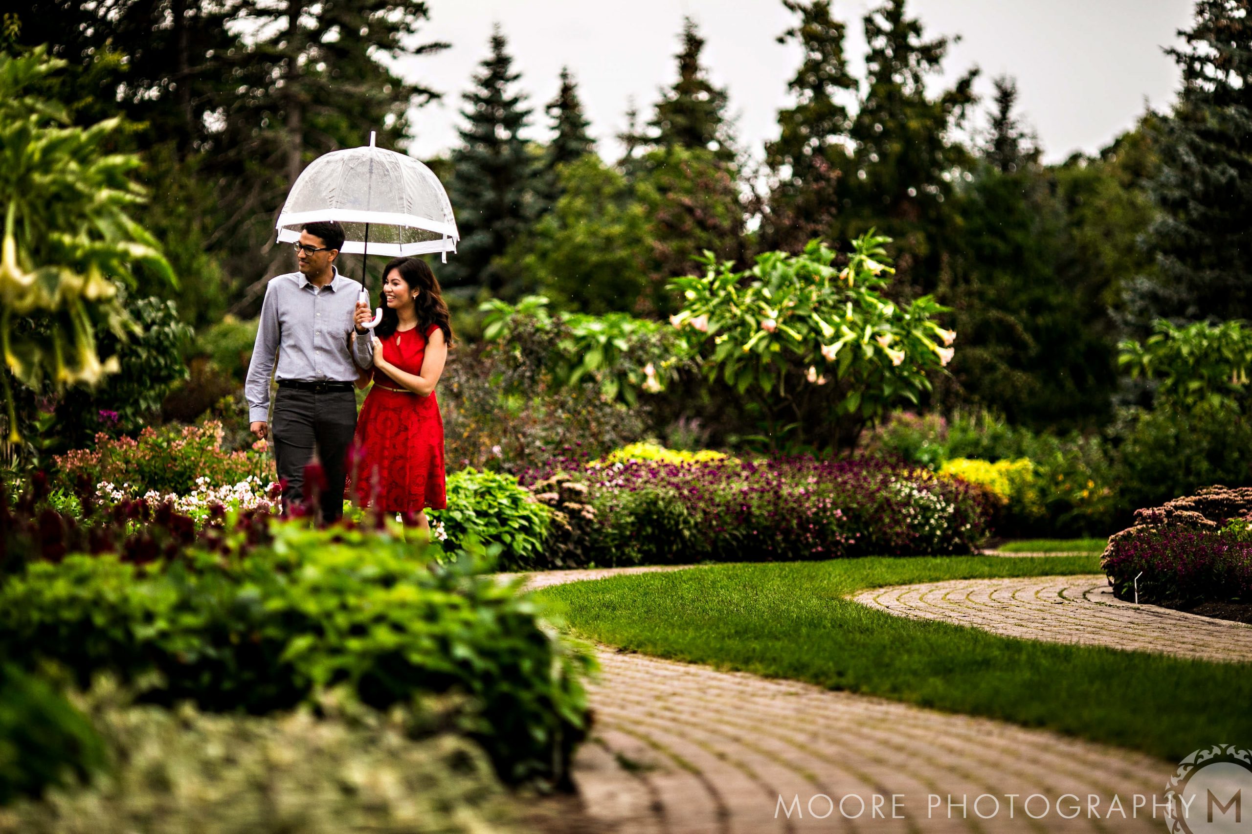 A relaxed couple strolling with an umbrella in Winnipeg's lush garden paths.