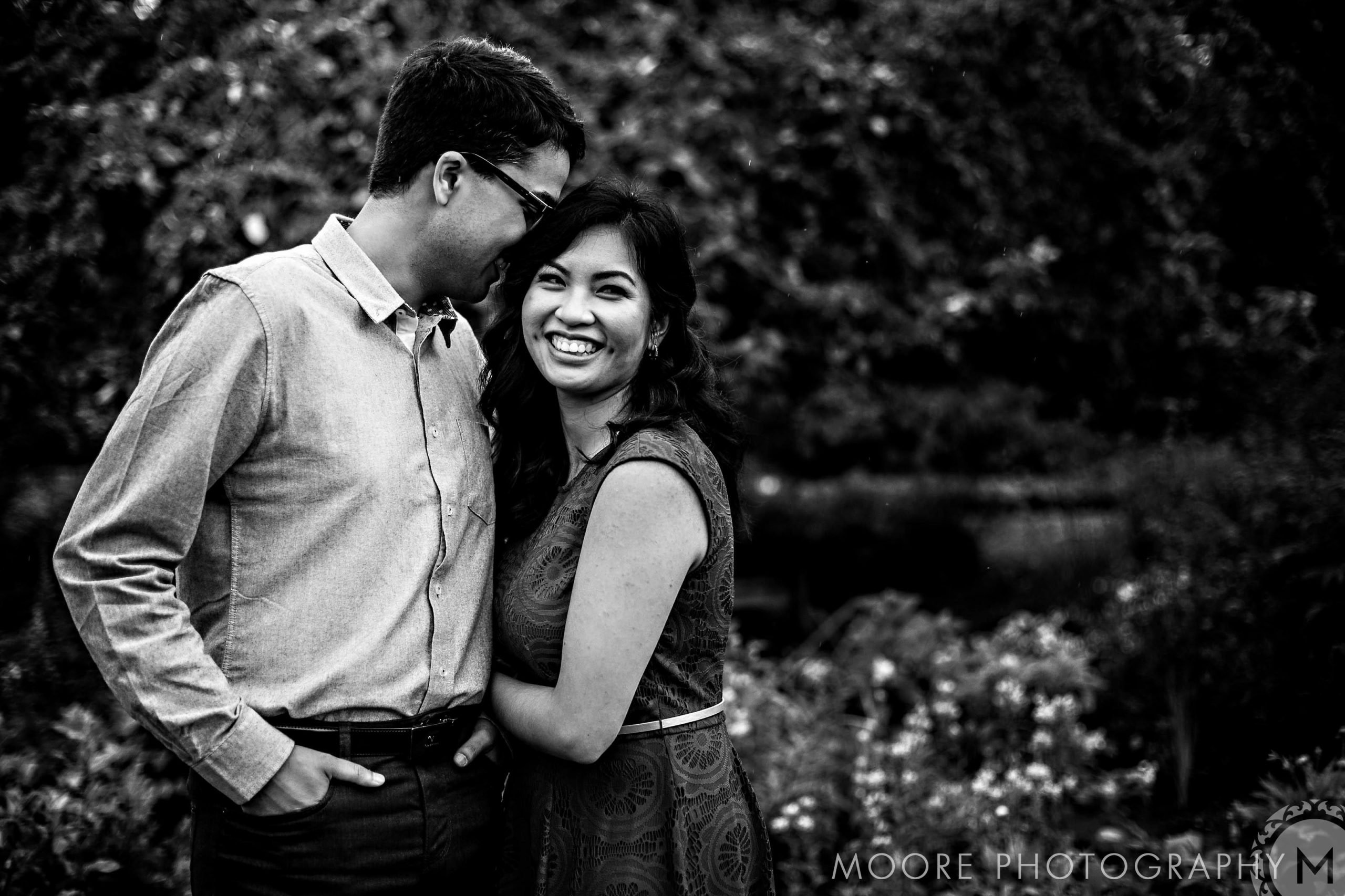 Relaxed couple smiling and embracing in a garden, Winnipeg engagement photo in black and white.