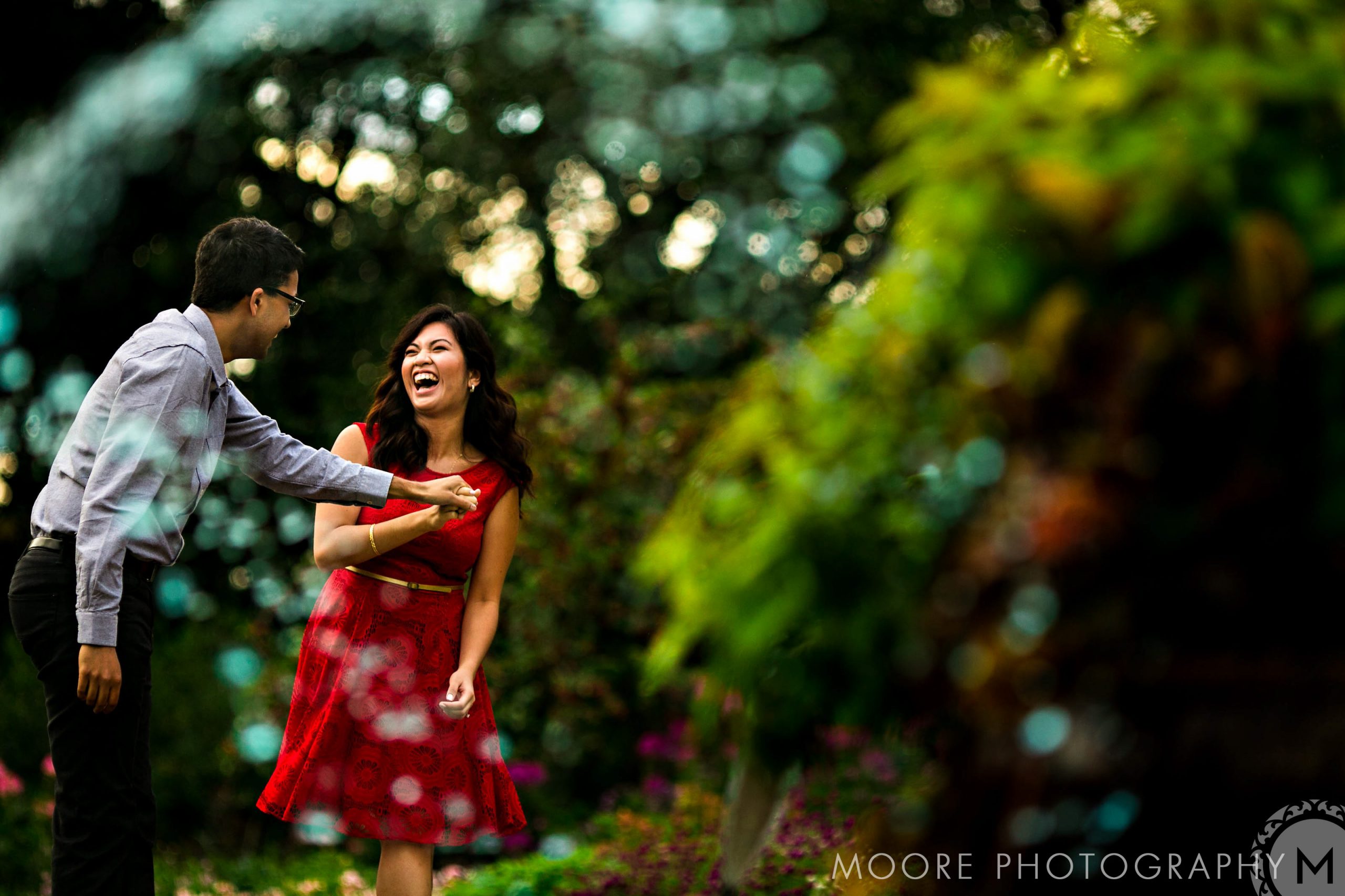 Relaxed couple laughing in a Winnipeg garden, surrounded by colorful, blurred foliage.