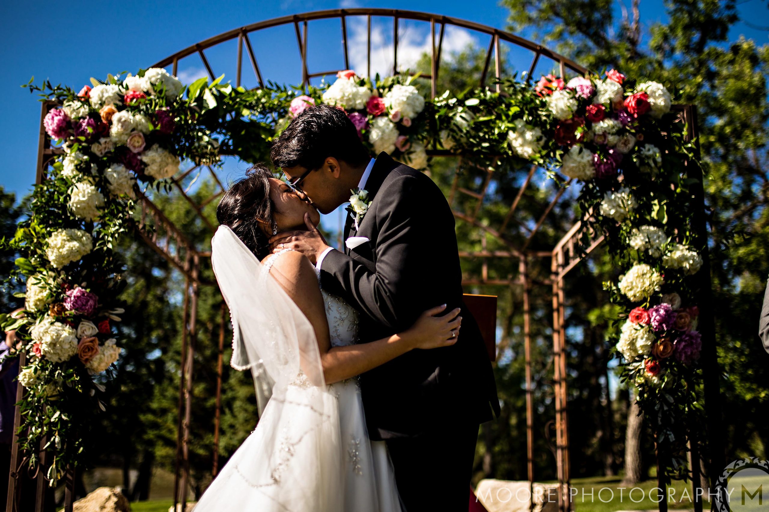 Bride and groom kiss under a floral arch at a top Winnipeg wedding venue.