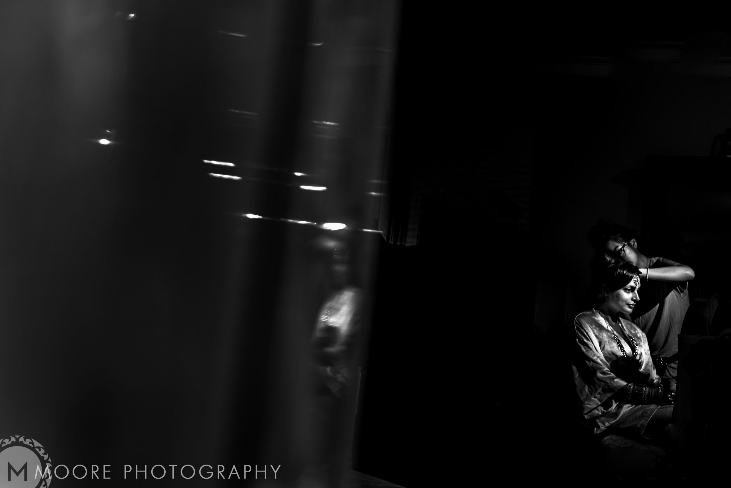 Black and white image of a person seated in a dim room, like a scene from an Indian wedding.