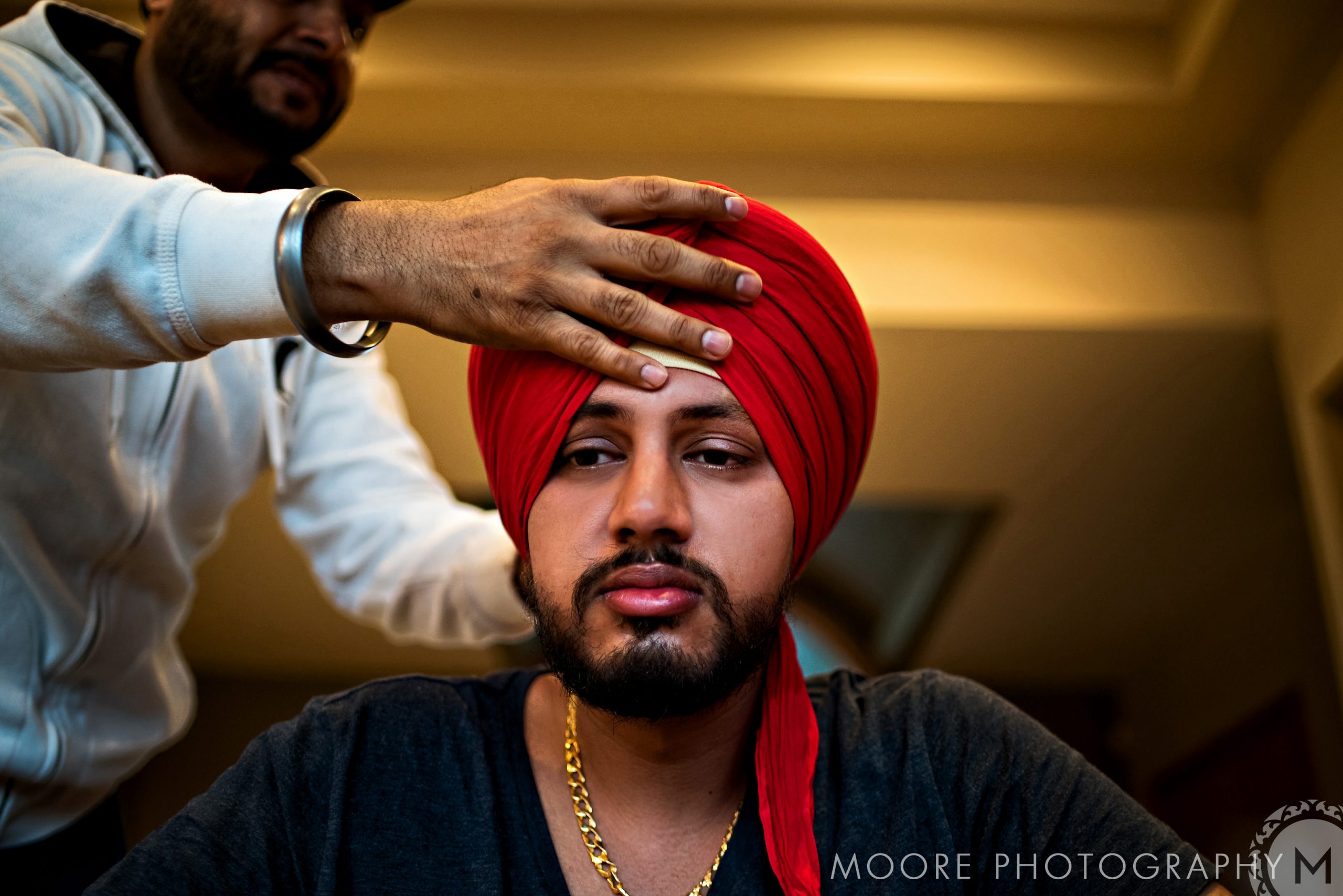Person adjusting a red turban for an Indian wedding indoors.