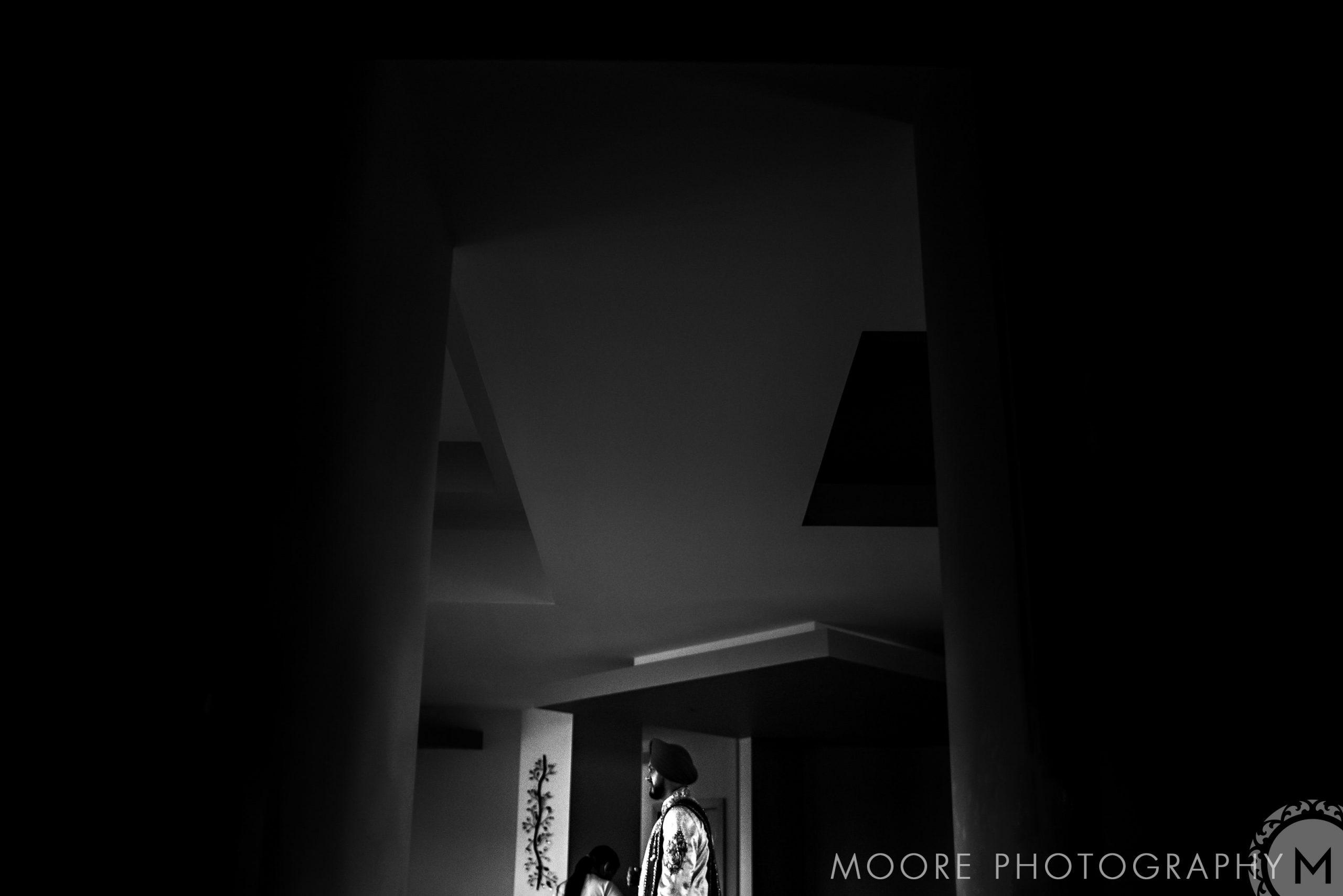 Silhouetted figure standing in a dimly lit, geometric room, evoking an Indian wedding aura.