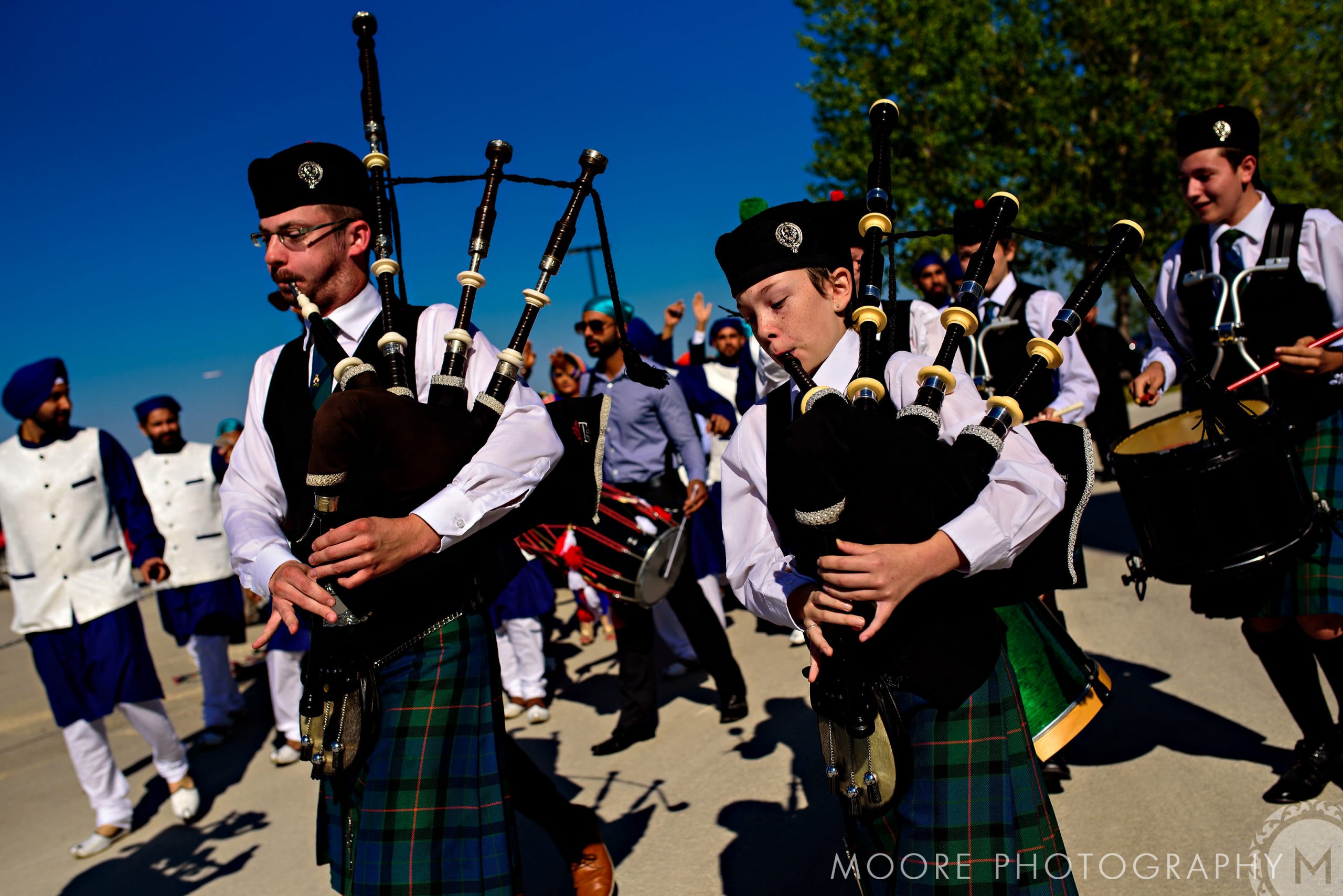 People in colorful attire play bagpipes and drums like an Indian wedding parade.
