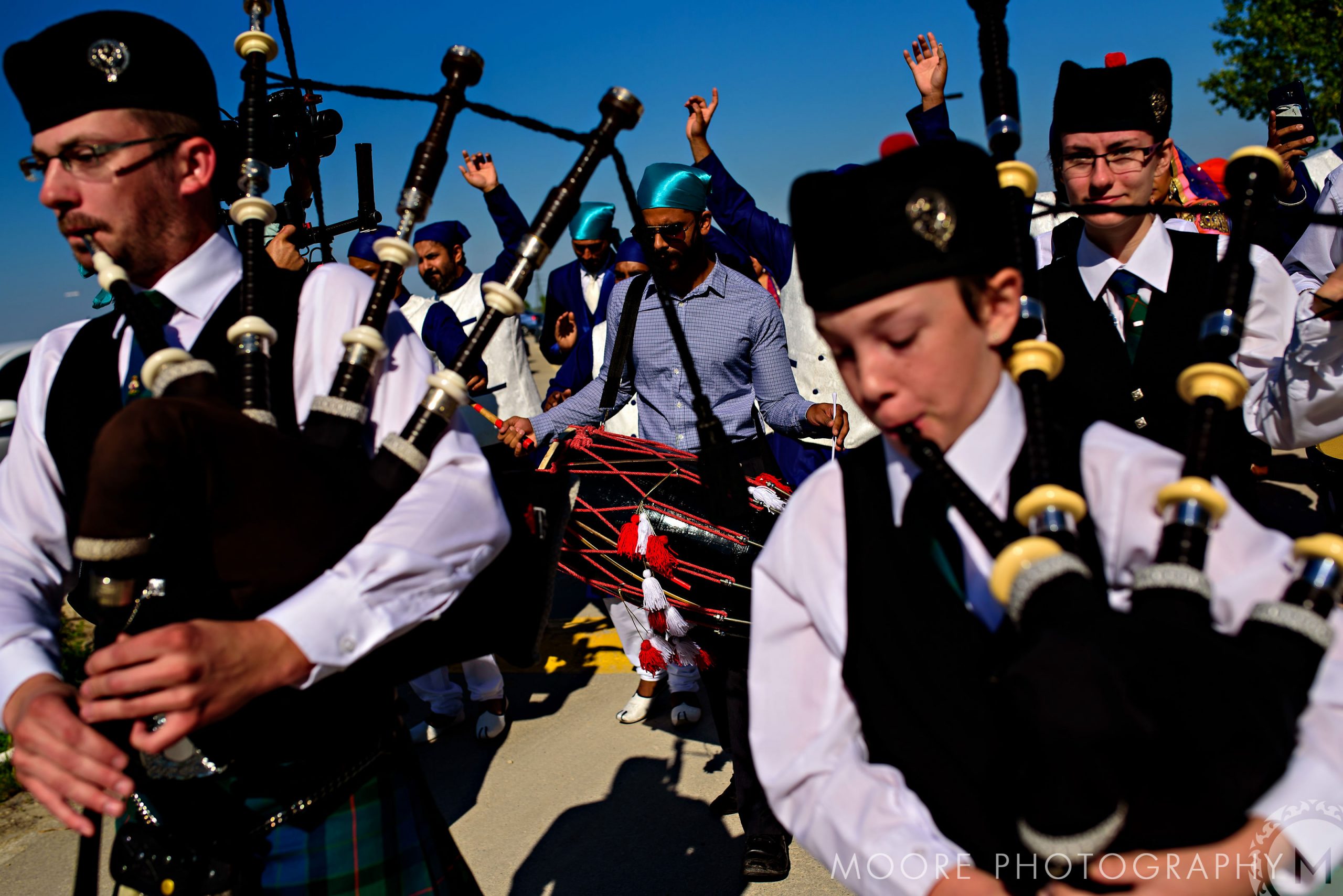 People playing bagpipes and drums at an Indian wedding under a clear blue sky.