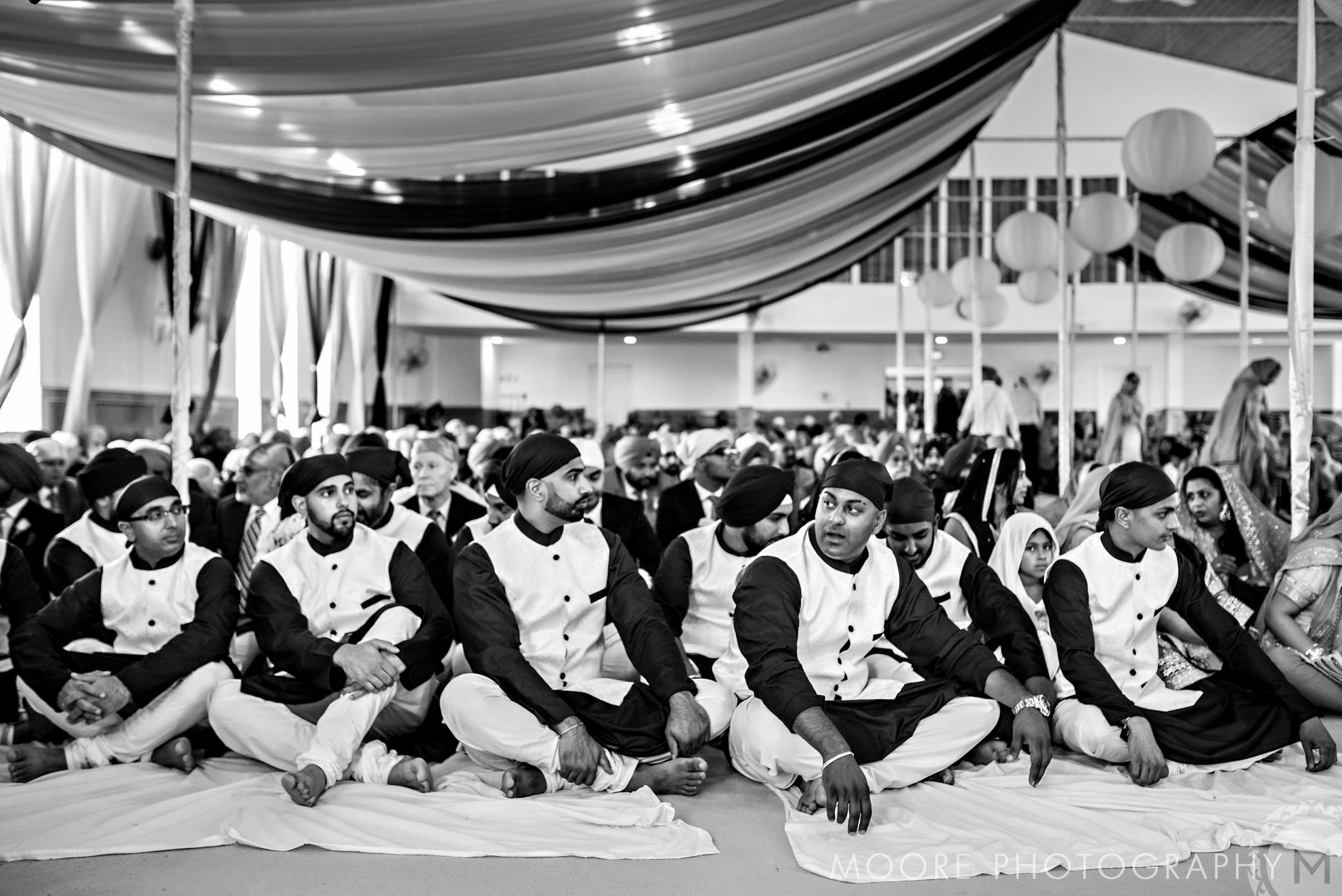 Group of people seated inside a beautifully decorated hall at an Indian wedding.