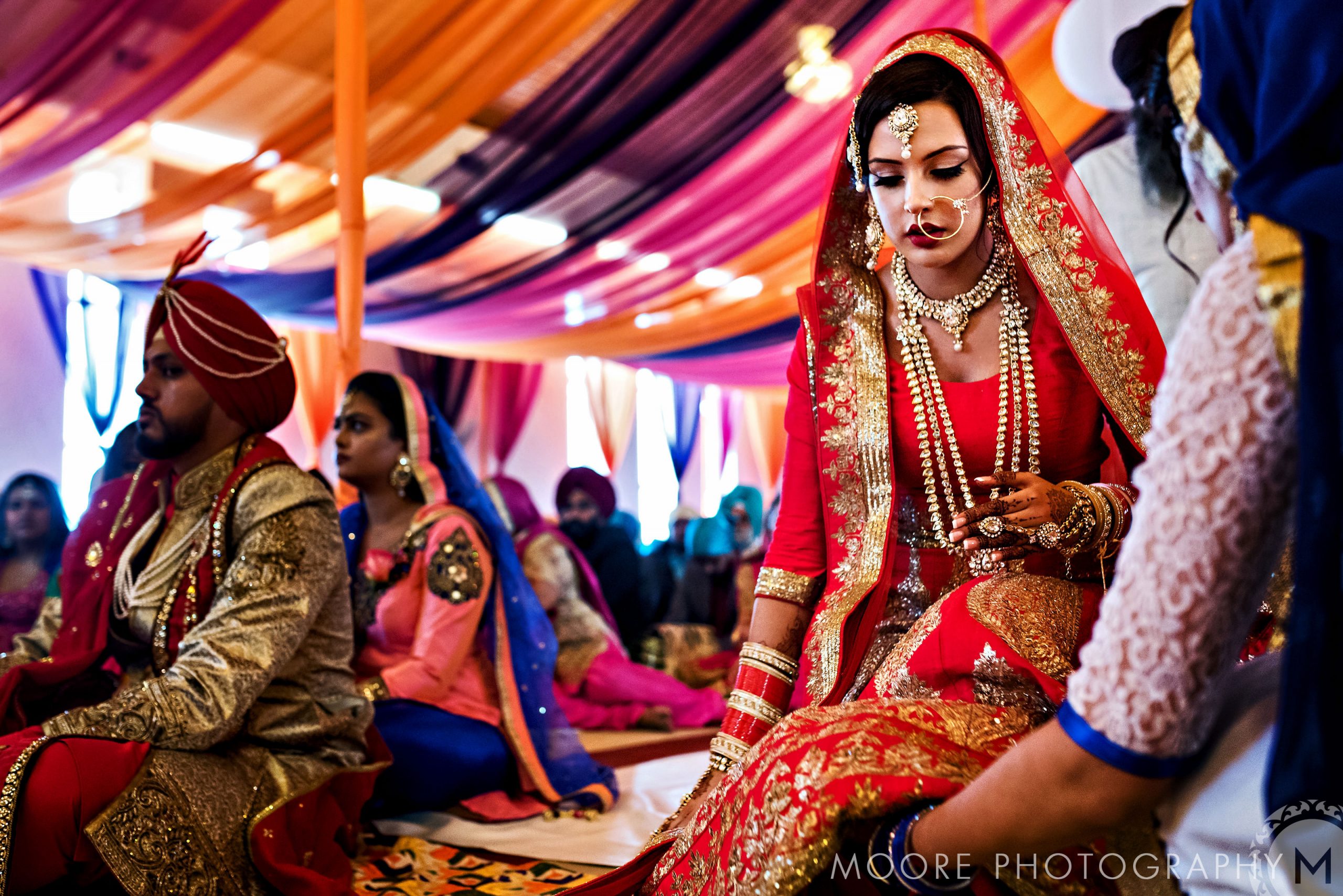 Bride in red and gold attire graces a vibrant, colorful Indian wedding ceremony.