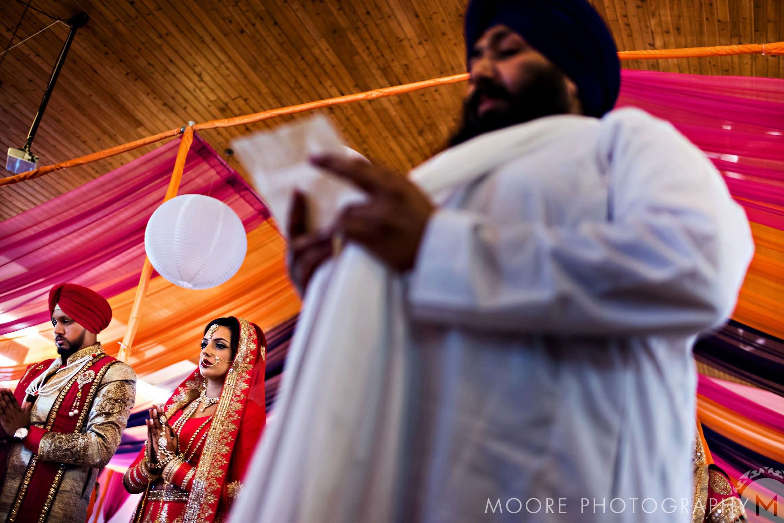 Indian wedding ceremony with couple and officiant under vibrant drapes.