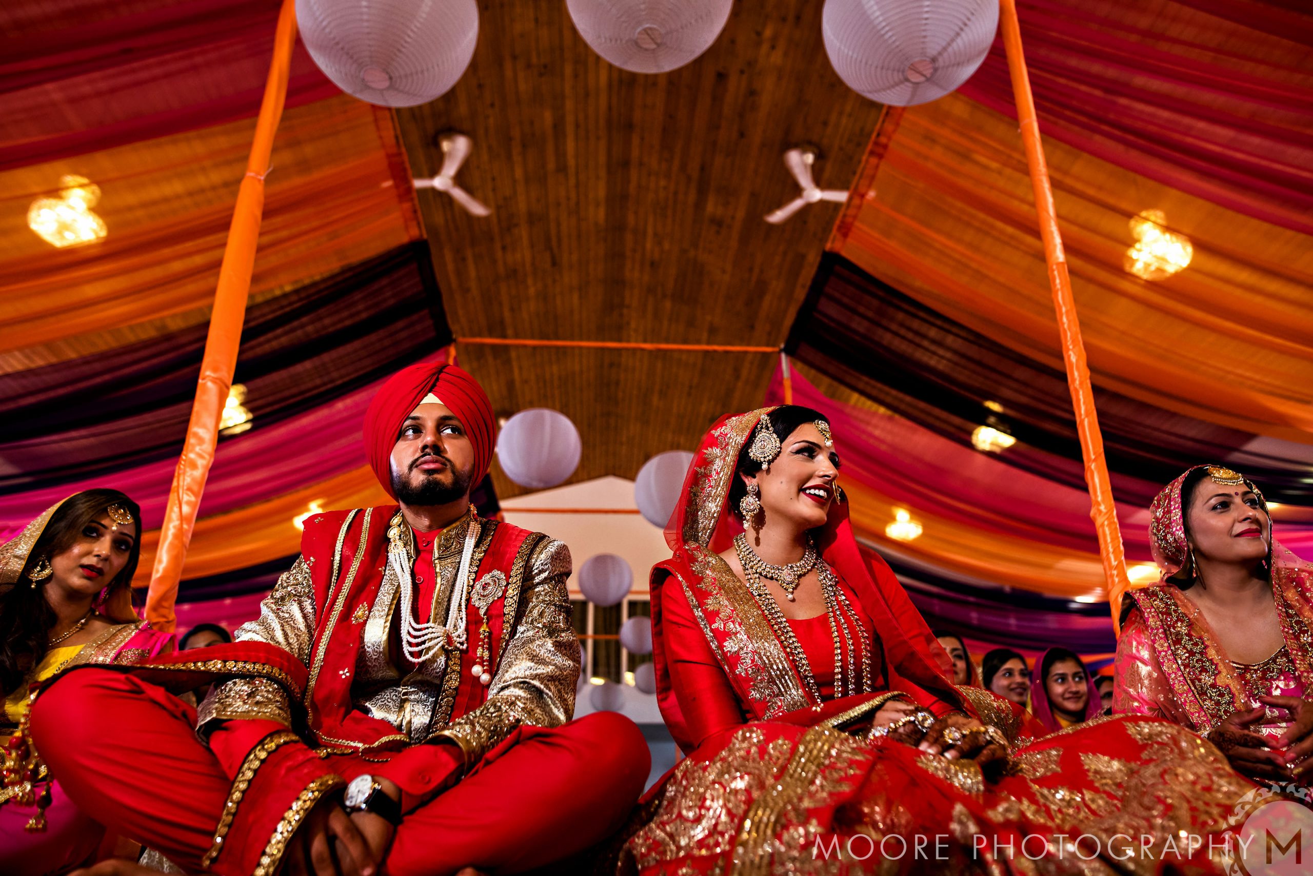 Bride and groom in traditional attire at a vibrant Indian wedding with draped decorations.