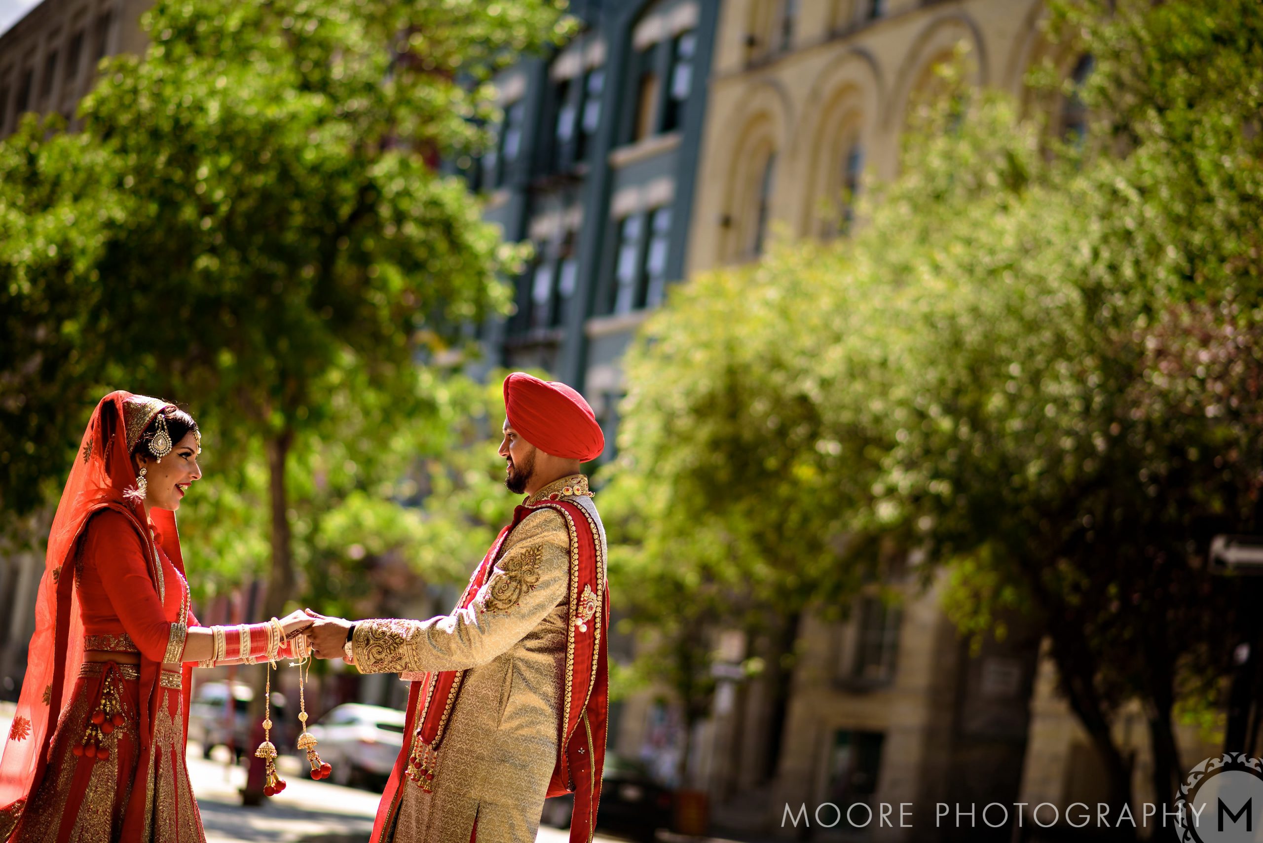 Indian wedding at the RBC Convention Center: couple in traditional attire holding hands in a sunlit urban setting.