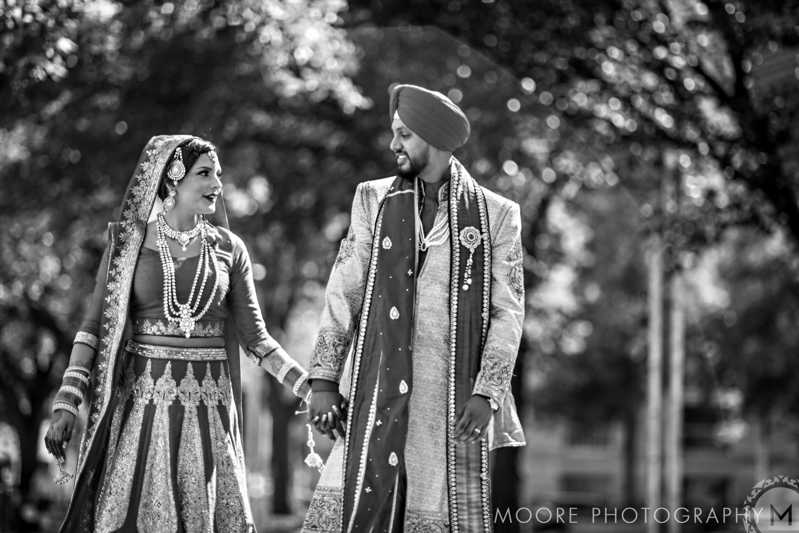Couple in traditional attire holding hands outdoors, smiling at each other during an Indian wedding.